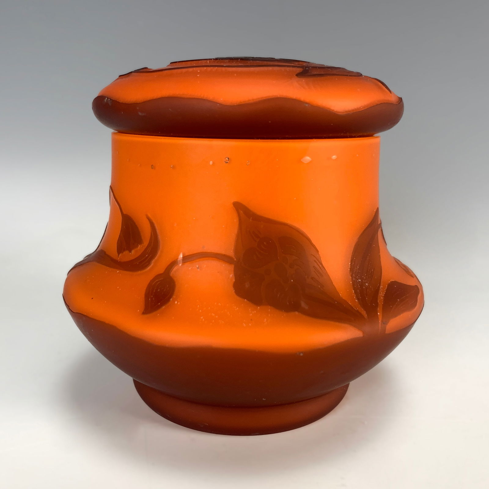 Loetz Cameo Glass Powder Jar: Wonderful cameo glass covered powder jar with an orange body and dark orange cameo leaves and flowers. Signed in cameo Loetz. Size: 4" tall x 4" wide. Condition: very good.