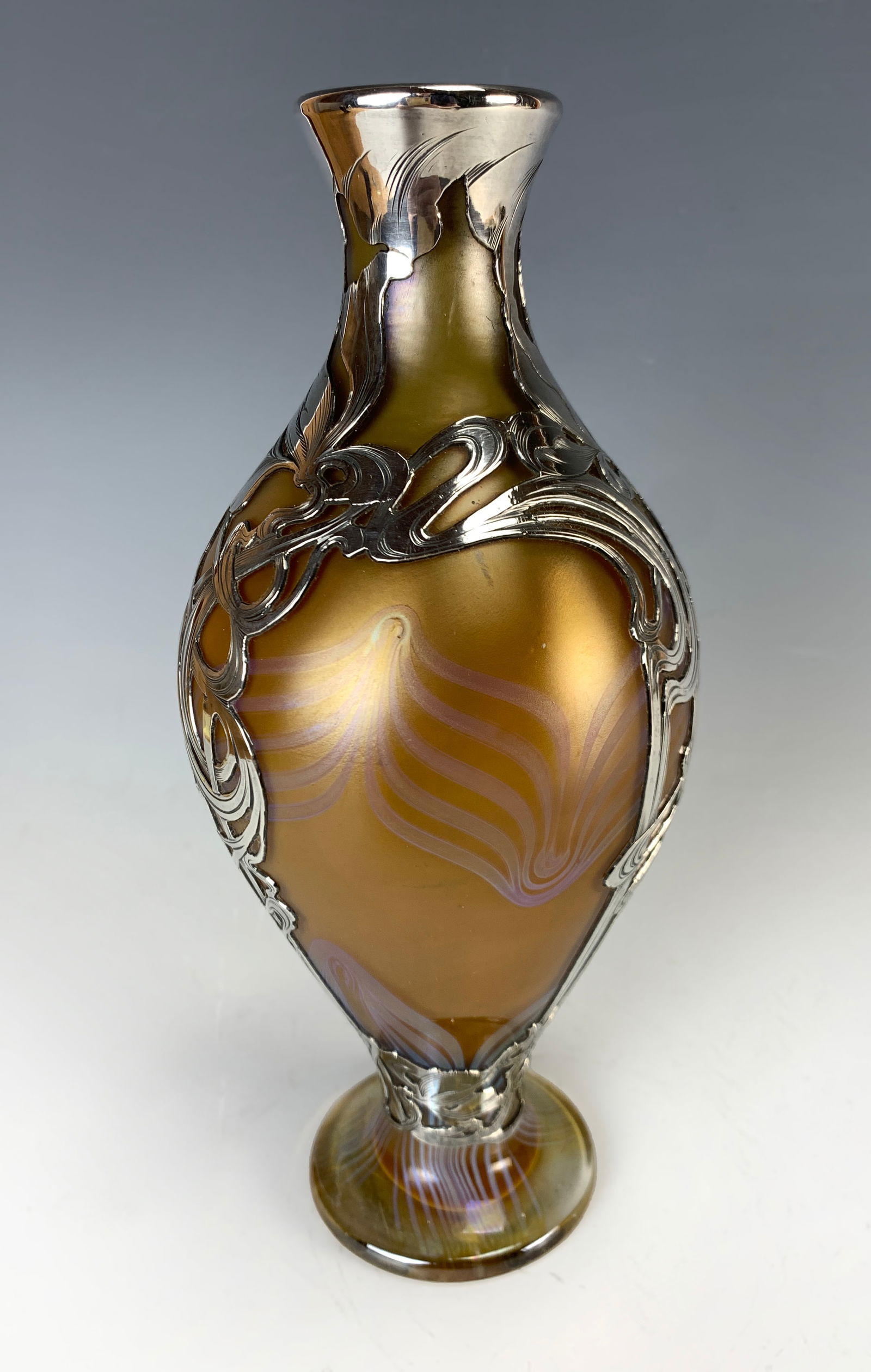 Loetz? Sterling Silver Overlay Vase: Having an amber feathered glass vase with sterling silver overlay. Marked "Sterling Silver Deposit." Size: 9" tall. Condition: Good.