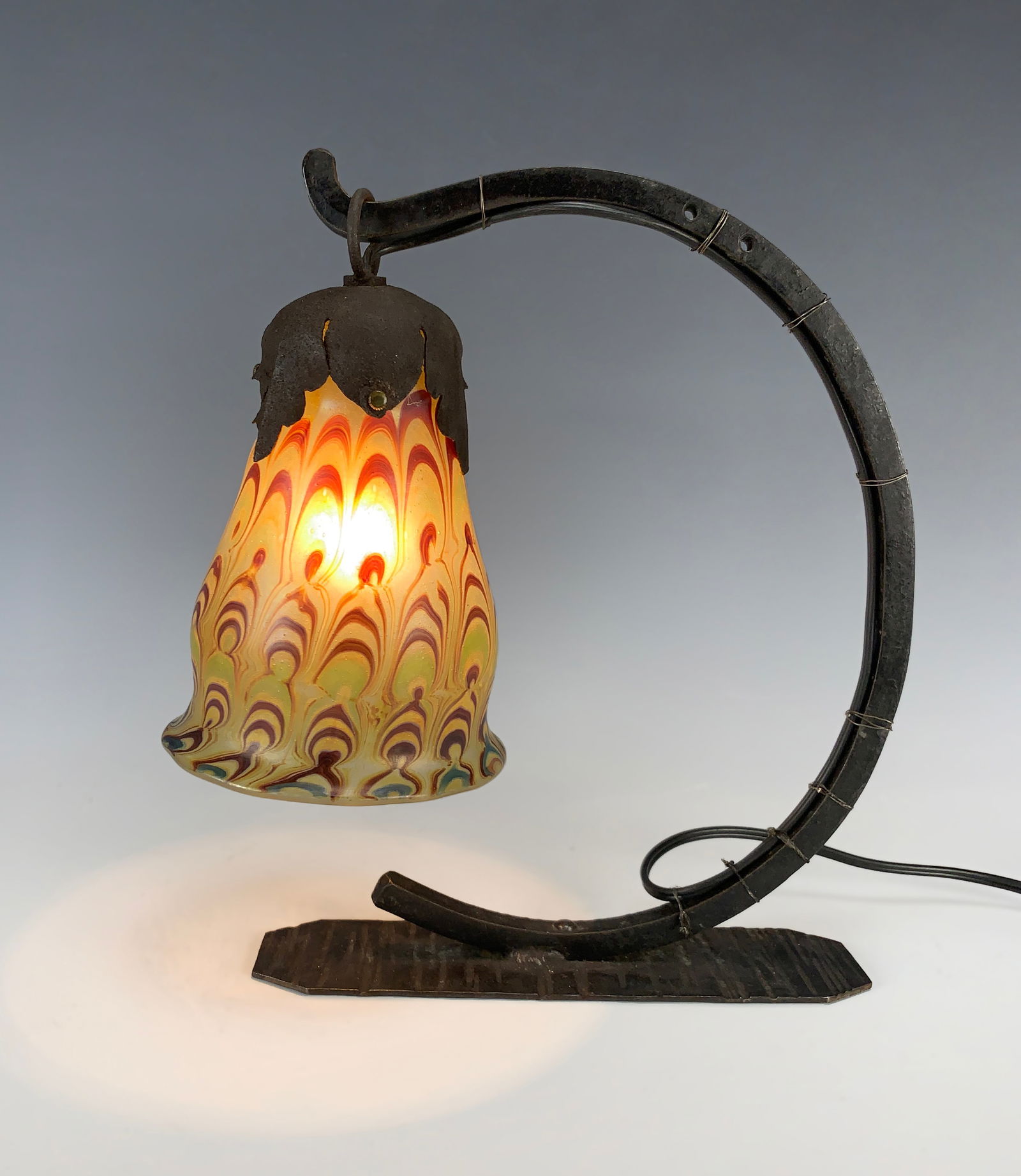 Loetz Style Small Desk Lamp w/Loetz Type Shade: Circa 1920s. Wrought iron desk lamp with an iridescent multiple swirl shade, Loetz style. Size: 10" tall x 9.5" wide. Condition: very good.