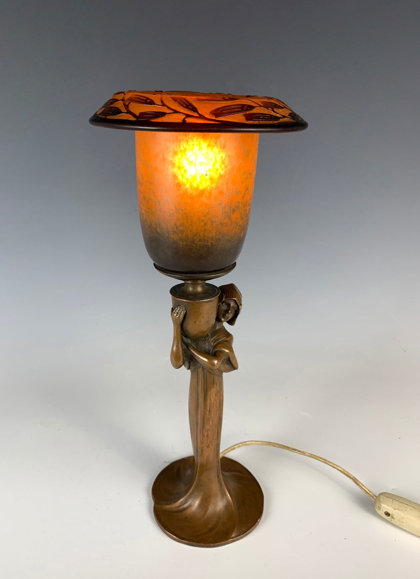 Daum Nancy Art Nouveau Figural Lamp: Circa 1900. Wonderful and all-original Art Nouveau lady figural lamp with a signed Daum Nancy cameo shade lamp. Shade in orange mottled glass and the bent rim in a cameo floral design. Size: 13.25" ta