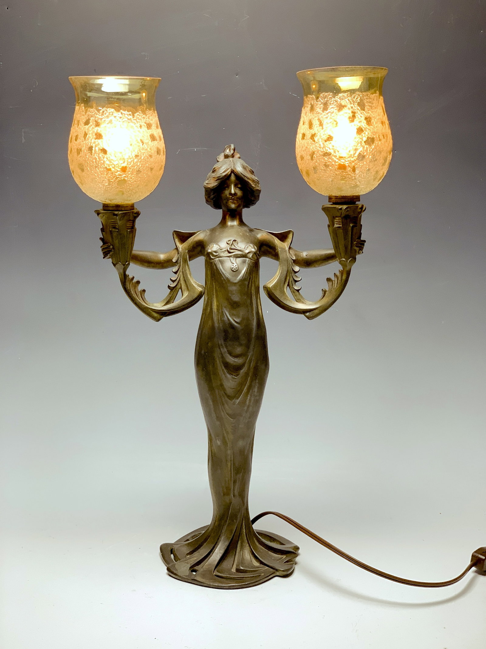 Lucien Alliot (1877-1967) Art Nouveau Lady Lamp: Circa 1900. Wonderful Art Nouveau lamp depicting a lady holding up in each hand matching original art glass shades. Made of spelter and done by well-known sculptor Lucien Alliot. Signed in the metal L