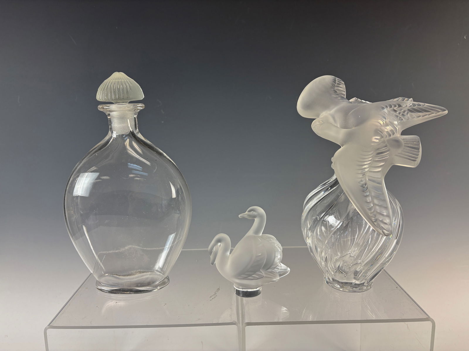 3 Sgd Lalique Items Perfume, Paperweight & Bottle: Lot of three signed Lalique items includes a Nina Ricci L'Air du Temps perfume bottle with two doves(7.5"), paperweight with two swans, a Guerlain perfume bottle, all signed "Lalique" tall very good c