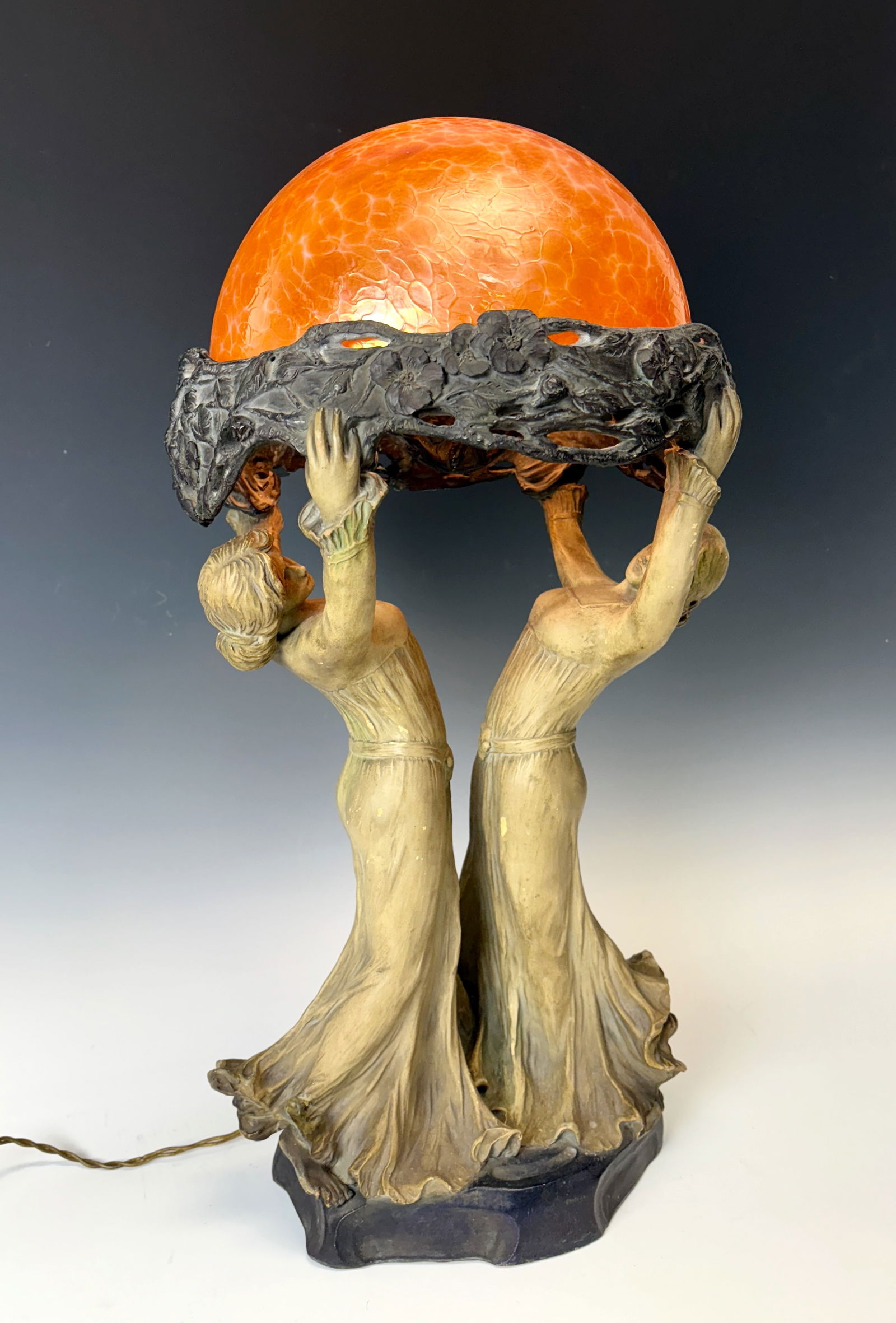 Jugendstil Figural Lamp w Iridescent Shade: Circa 1900, likely Austrian and attributed to Goldscheider, period Art Nouveau earthenware lamp depicting two opposing beauties with upstretched arms supporting an iridescent orange Loetz type art gla