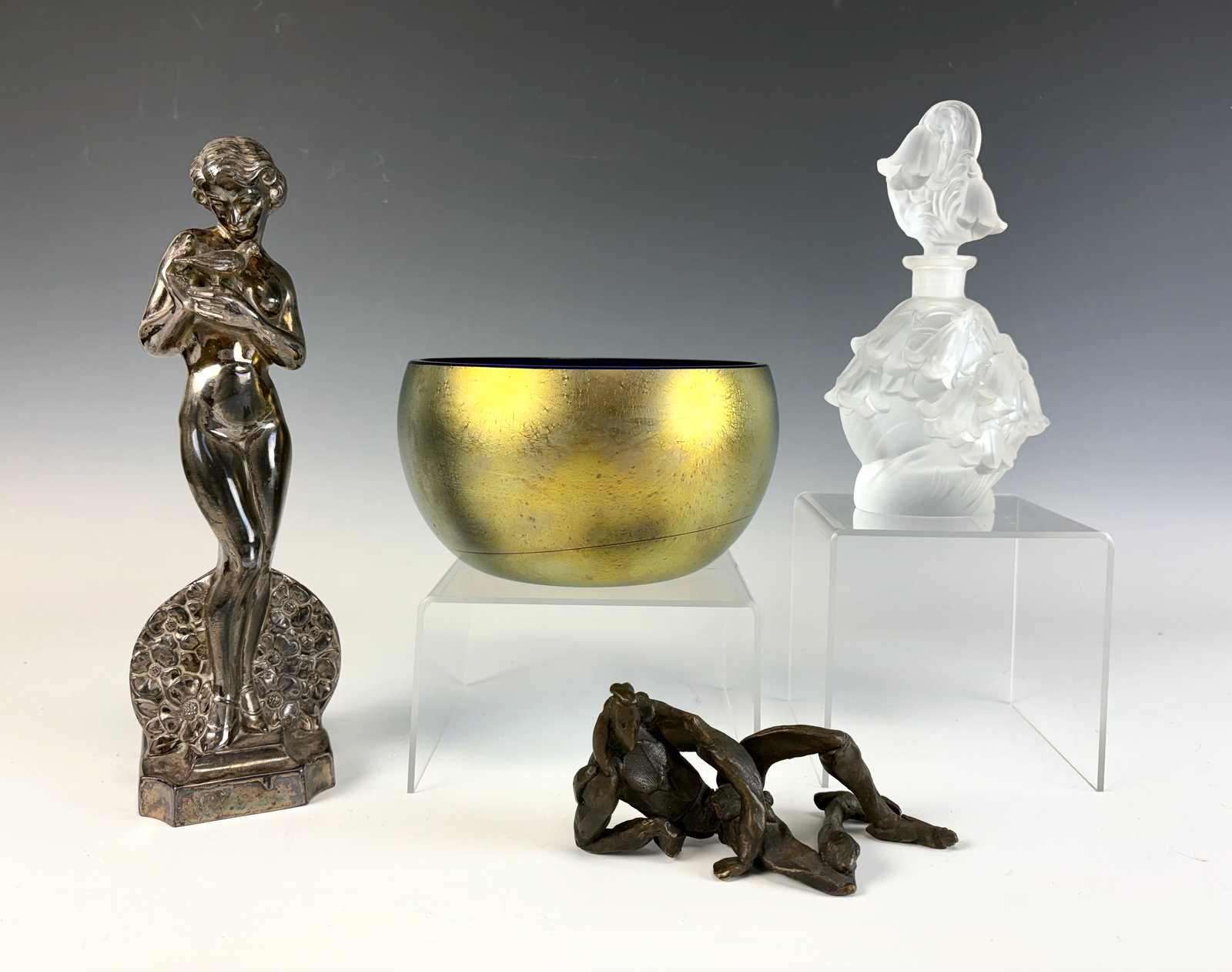 Group Lot: Perfume Bottle, Figurines, Iridescent Bowl: This group includes a signed Maslach ’83 gold iridescent bowl, a frosted glass perfume bottle signed DeNa, an abstract sculpture, and a silvered figure of a nude lady holding a bird. In good conditi