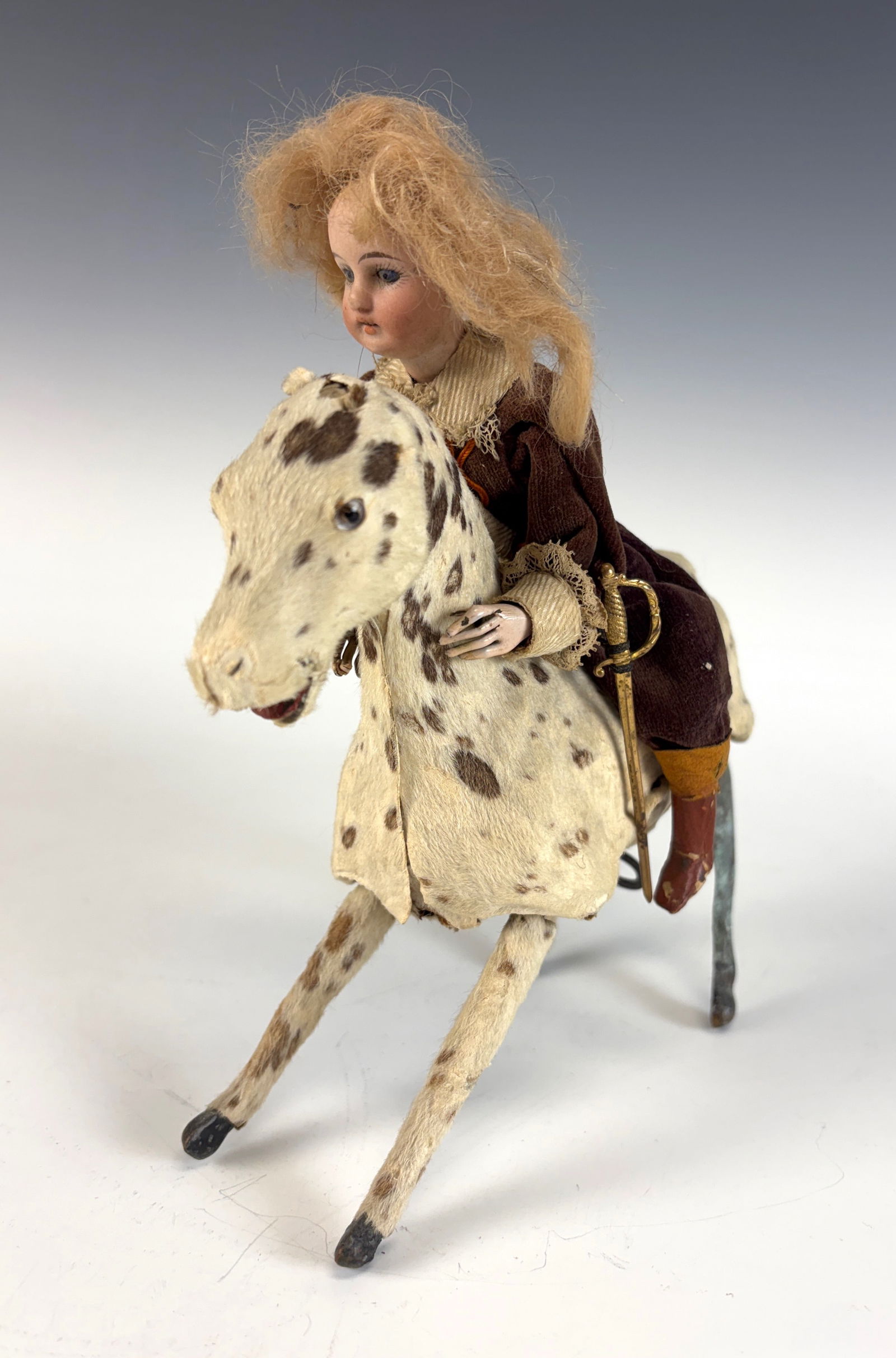 Antique Bisque Head Doll Riding Wind-Up Horse: A bisque head doll girl mounted on a calico wind-up horse, dating to circa 1900. The horse is missing its ears, and the wind-up mechanism works but needs attention. Selling as-is; with careful restora