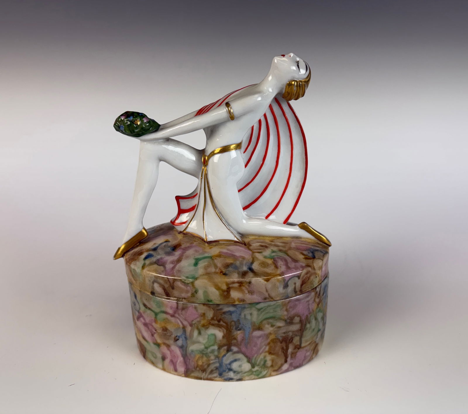 Art Deco Porcelain Powder Jar: A charming art deco porcelain powder jar featuring a lady figural on the top, dating to circa 1920s. 6.5” tall × 4.5” wide × 3.25” deep. In excellent condition.