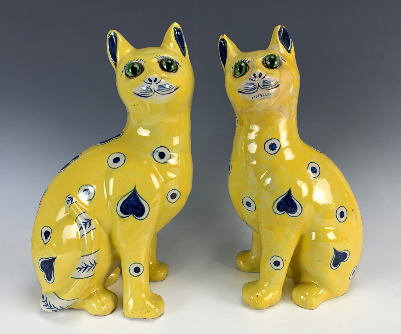 Pair of Galle Yellow Faience Seated Cat Figurines: Pair of authentic antique Galle yellow faience seated cats with applied glass eyes, decorated with blue and white hearts on a yellow ground. Each signed E. Galle Nancy. These are not copies but