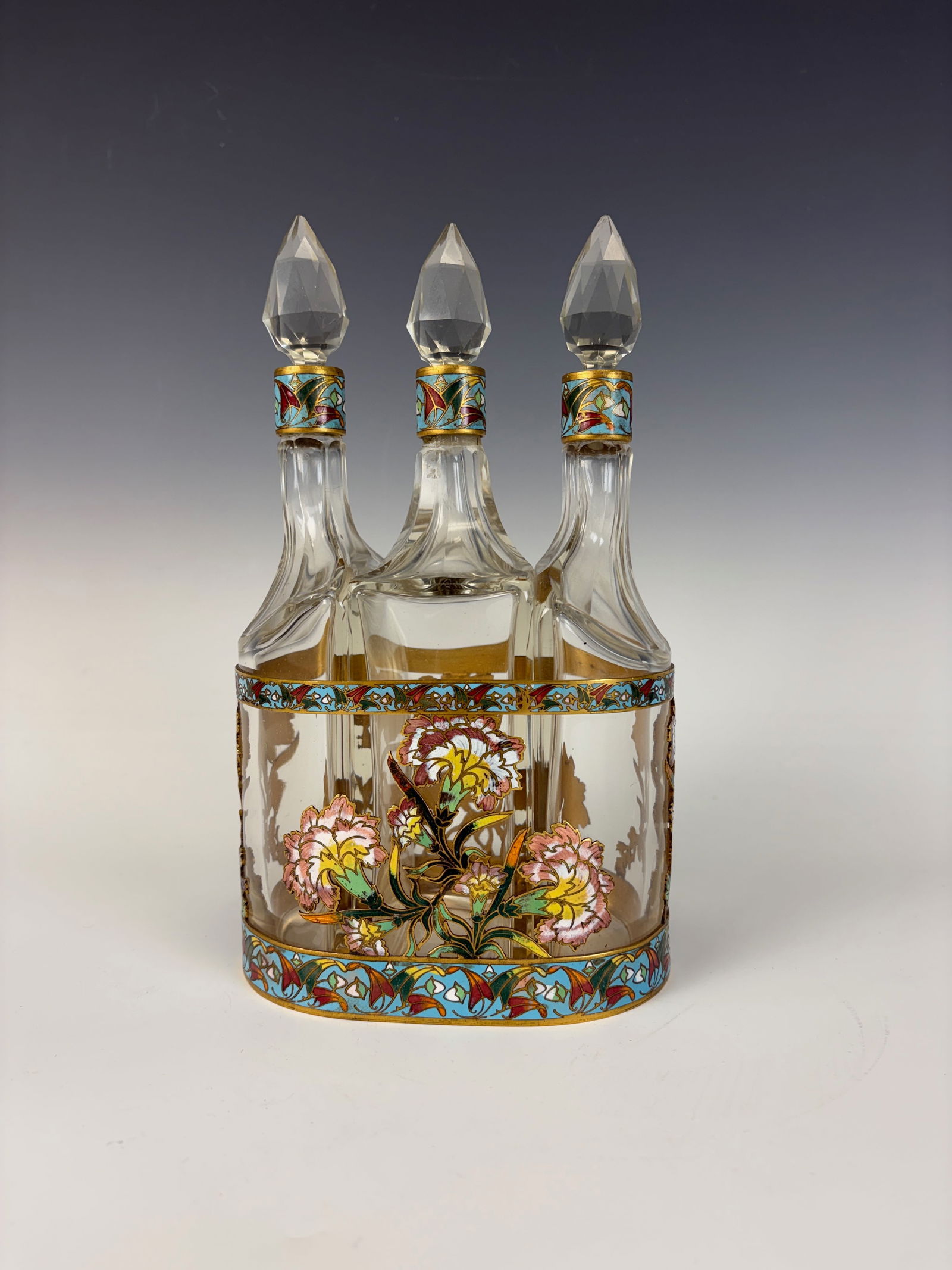Bronze & Champleve Enamel 3 Bottle Liquor Set: circa 1900, unusual and elegant bronze and champleve enamel three bottle liquor set in matching enameled base, bottles with original faceted cut glass stoppers, beautiful detailed metalwork, very good