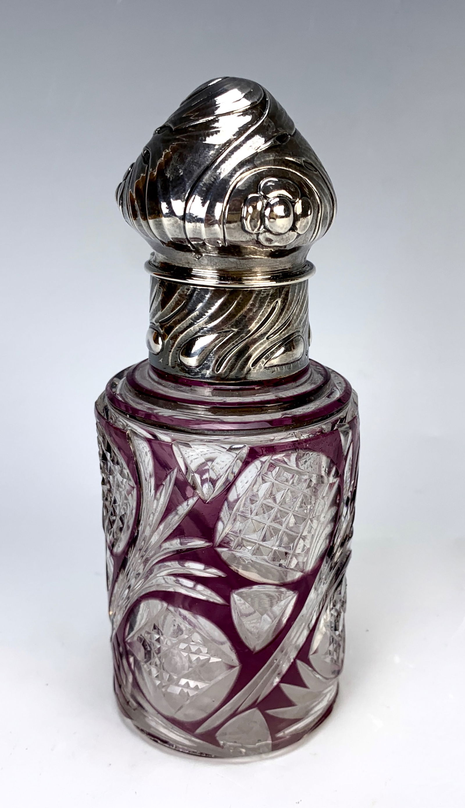 Antique Amethyst & Clear Cut Glass Sterling Perfume Bottle: Late 19th century, a cylindrical body in clear cut glass with amethyst overlay, a sterling ornate dome top lid and collar, includes the original stopper, glass is signed with a letter "M" within AM,