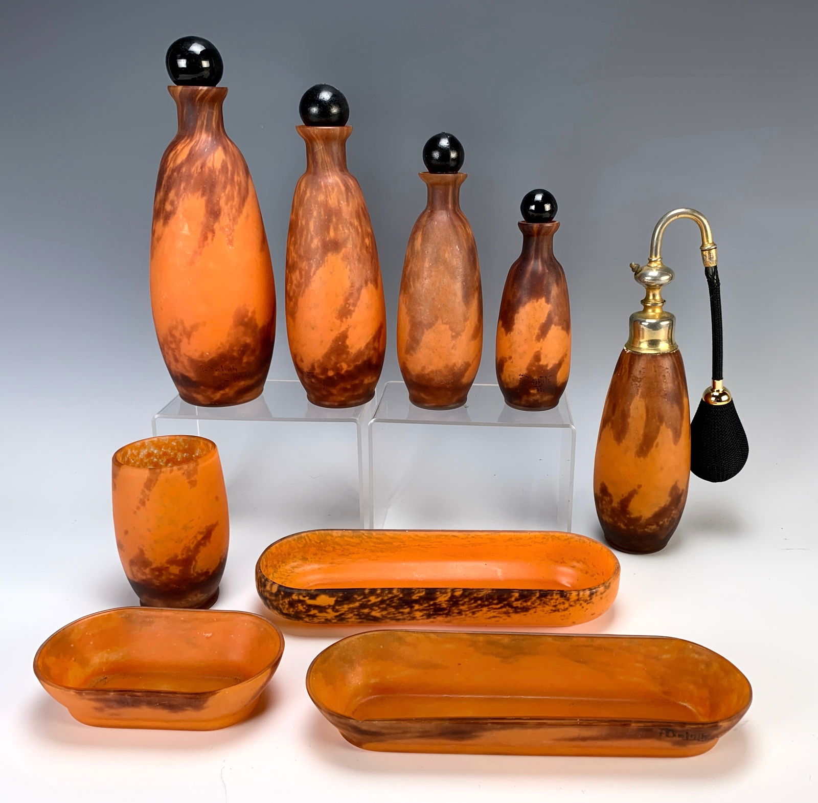 Delatte Nancy 9 Pc Art Deco Vanity Set: Circa 1920, very nice French art glass ladies' vanity set consisting of 4 bottles, 3 trays, a cup and a perfume atomizer, all in orange mottled glass, with 6 signatures still visible. 9" tallest