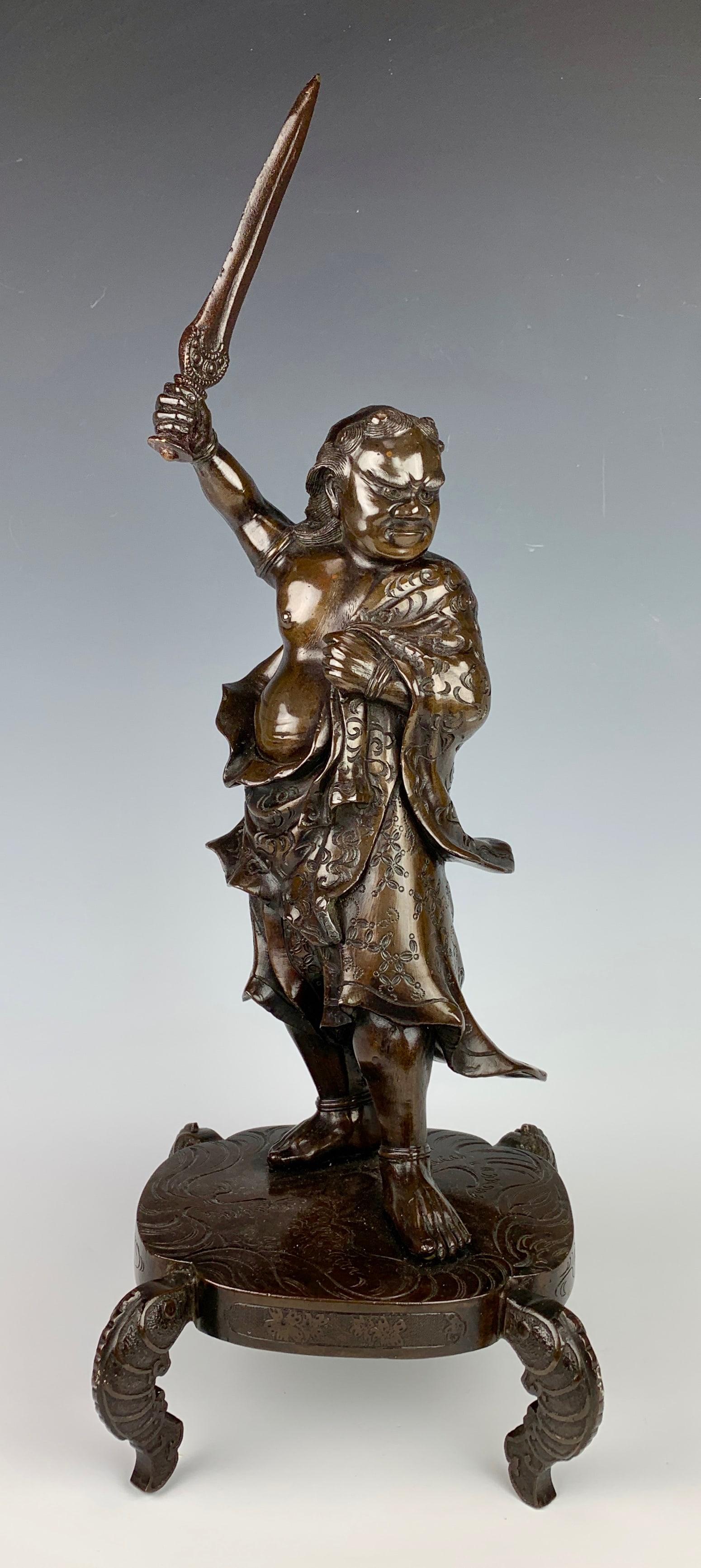 Japanese Bronze Fudo Myo-O Okimono, Meiji Period: Meiji period (1868-1912), the buddhist guardian deity standing with his left foot forward and brandishing a sword in a defying stance, wearing a skirt decorated with shippo patterns and holding his
