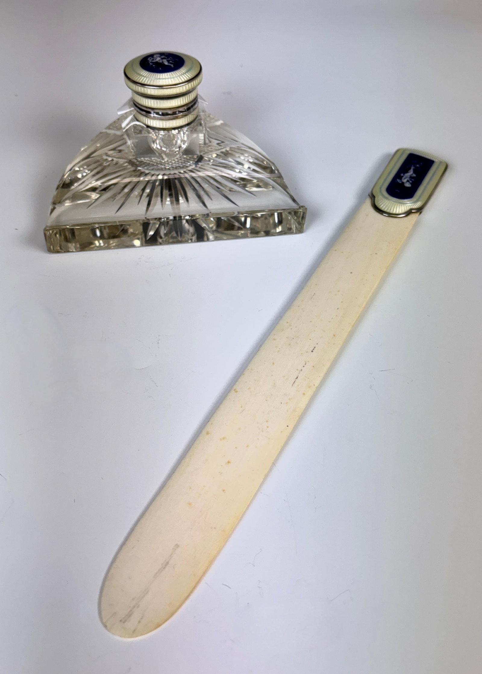 Enamel & Sterling Silver Inkwell & Letter Opener: Included in lot is a clear glass inkwell with yellow and blue enamel lid and blue enamel central element with a cherub, with a matching letter opener having a bone blade and yellow and blue enamel