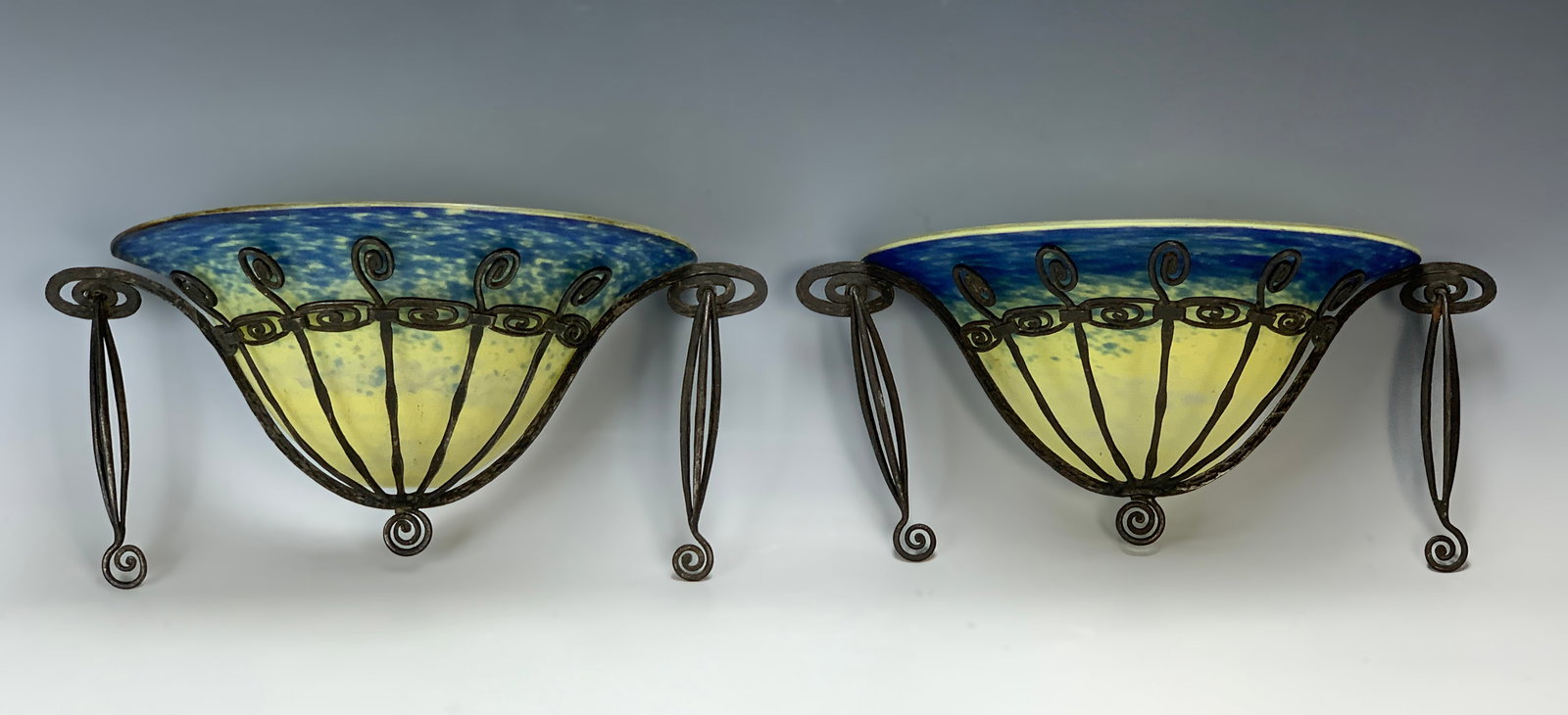 Pair Sgd Schneider Art Deco Glass & Iron Sconces: Circa 1920s. Having a nice pair of Art Deco wrought iron sconces in the form of half baskets with a scroll design. Featuring mottled glass shades in colors of yellow and blue, each signed Schneider. 1