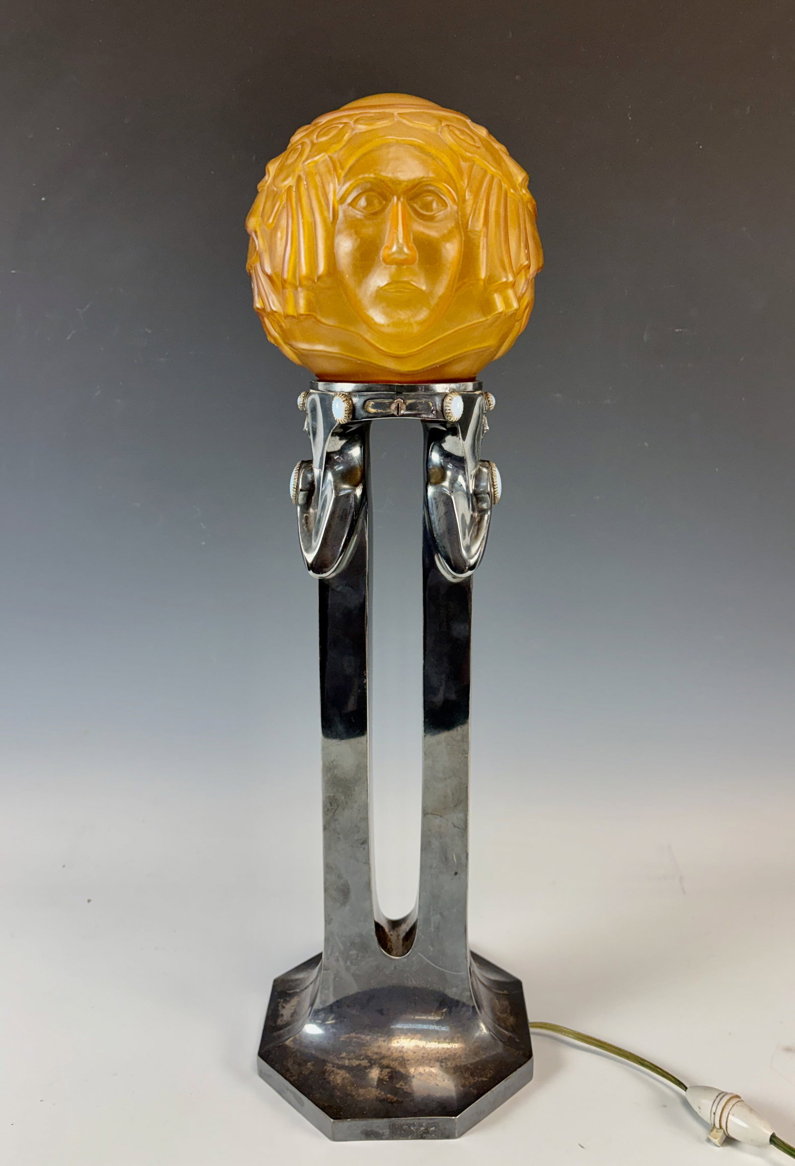 Silvered Art Deco Lamp with Egyption Herms & Faces: Circa 1920, a silverplated art deco lampbase with glass shade with faces, base characterized by two stylized Egyptian herms embellished with 8 embedded oval opaque jewels, the art glass shade with
