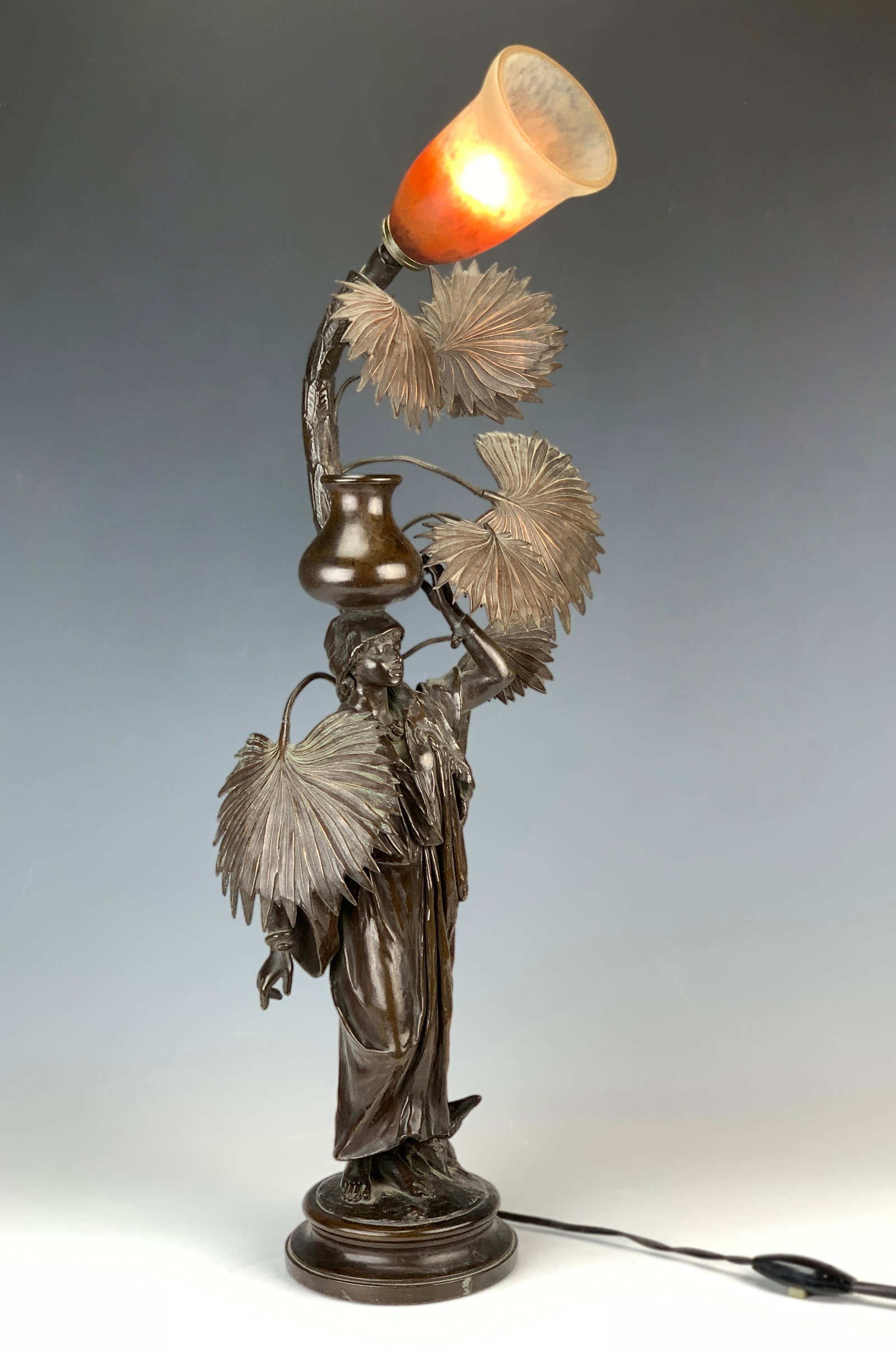 Sgd Schneider Bronze & Art Glass Orientalist Lamp: Circa 1910, fabulous patinated bronze and art glass lamp with an orientalist figural base with a woman carrying a jug and palm tree; base supports a signed Schneider orange mottled glass shade. 25"