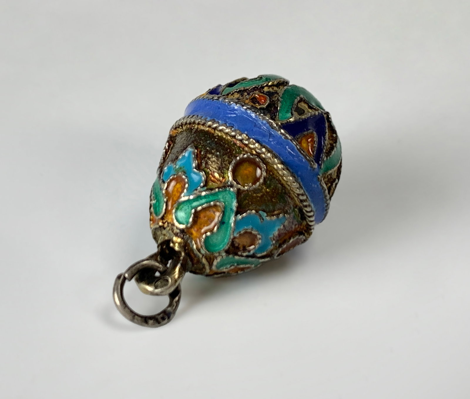 Russian Silver & Enamel Egg Charm: A small silver egg charm decorated in colors of green, amber, blue, and turquoise enamels. Partial hallmark on the silver ring. very good condition, 17mm x 13mm.
