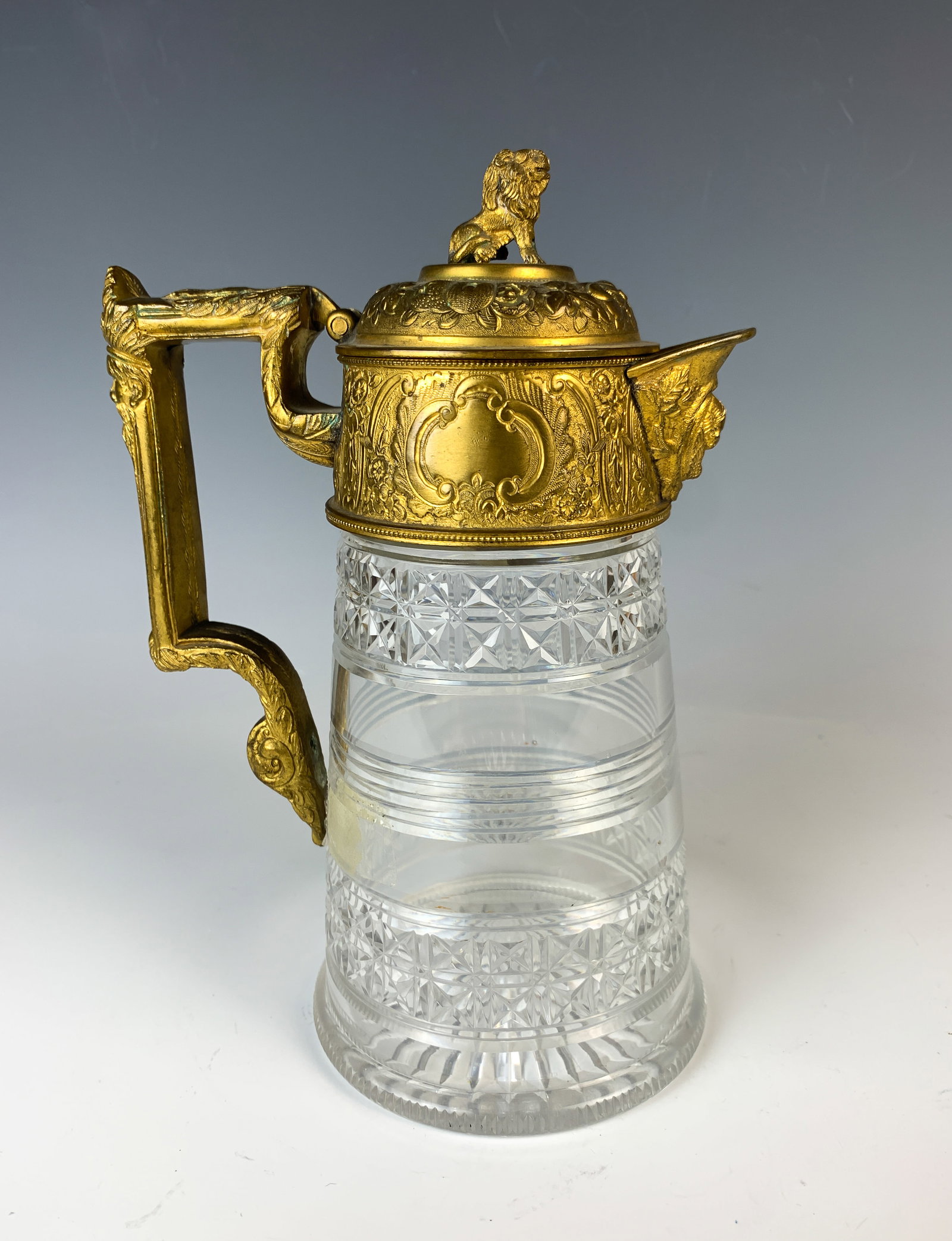 Antique Gilt Bronze & Cut Glass Pitcher: Late 19thC. Cut glass body with gilt bronze hinged lid. Top of lid decorated with a sitting lion, handle decorated with face of bearded man, and a winged cherub on spout, good codition, wear to gilt