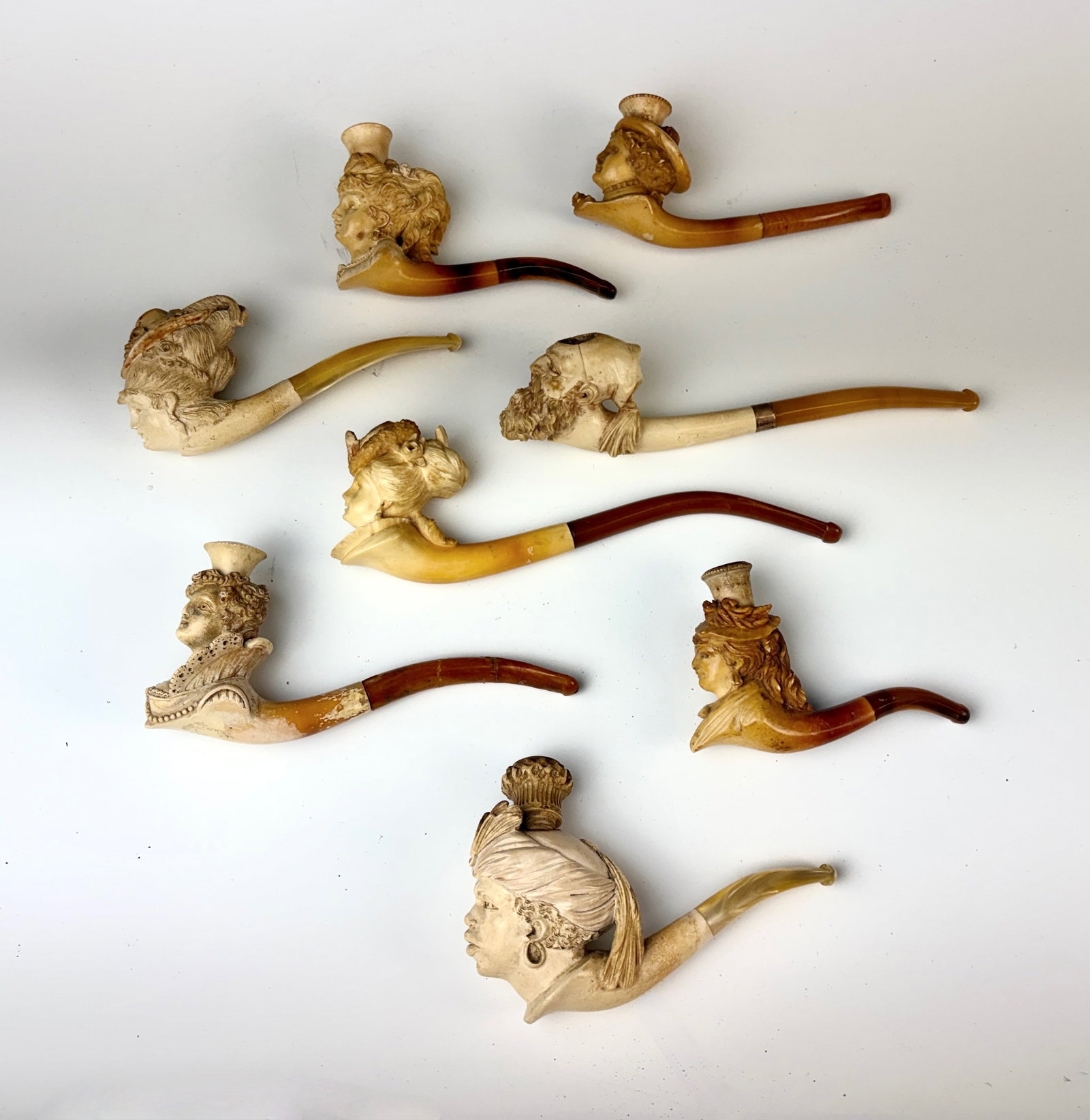 Group of 8 Figural Meerschaum Pipes: Circa 1880, group of Meerschaum pipes modeled as busts of young ladies and one man, various elegantly coiffed and adorned profiles, some with hats or headdresses, amber stems, one stem reglued,