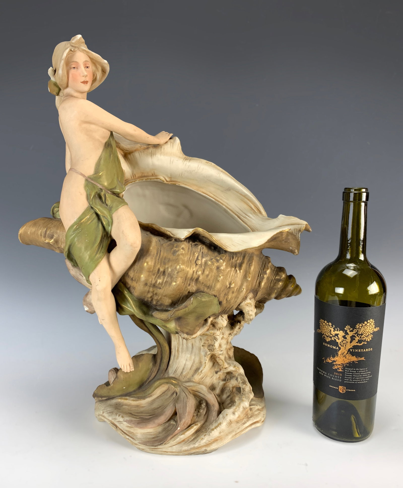 Large Royal Dux "Nymph & Conch Shell": Circa 1900. Wonderful porcelain Art Nouveau figure of a nymph sitting on the side of a conch shell. Dated 1905, and initials HS. Signed with pink applied triangle mark, both thumbs are broken.18.5" ta