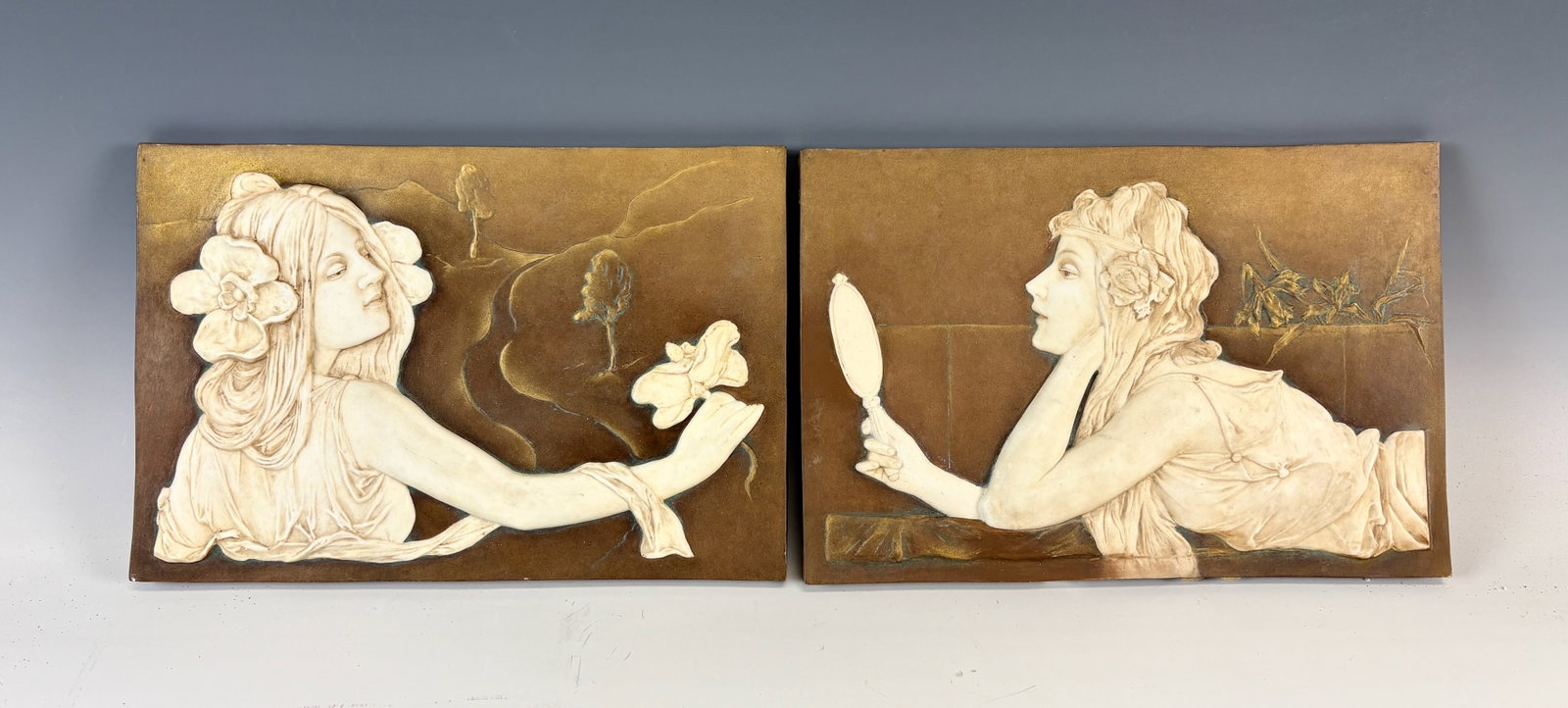 Pair Art Nouveau Porcelain Plaques: Circa 1900, old and original period art nouveau raised relief porcelain plaques, both tinted white against sepia backgrounds, both with beautiful females, one gazing at herself in a mirror, the other 