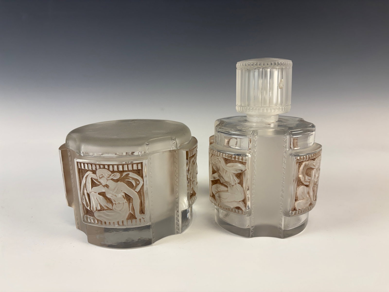 Lalique St. Helene Perfume Bottle & Powder Box: Circa 1942, a clear and frosted glass St. Helene perfume bottle and powder box with sepia patina, powder box with chips on interior rim edge, otherwise both in good condition, tallest 5.5"