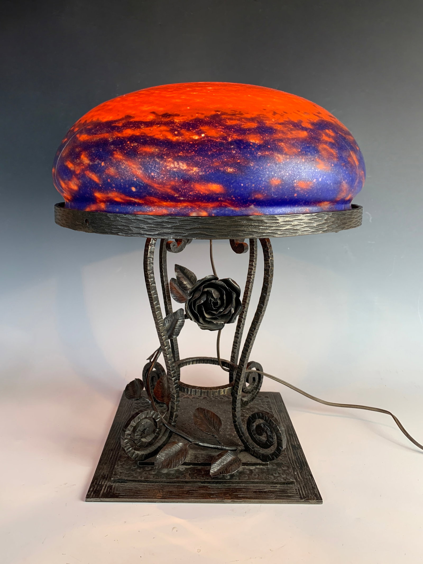 Muller Fres Luneville Art Deco Lamp: Circa 1920s. Attributed to Muller Fres. French mottled orange with blue mottling mushroom shade mounted atop a square wrought iron base decorated with flowers and leaves. Size: 17.5" tall x 14" at wid