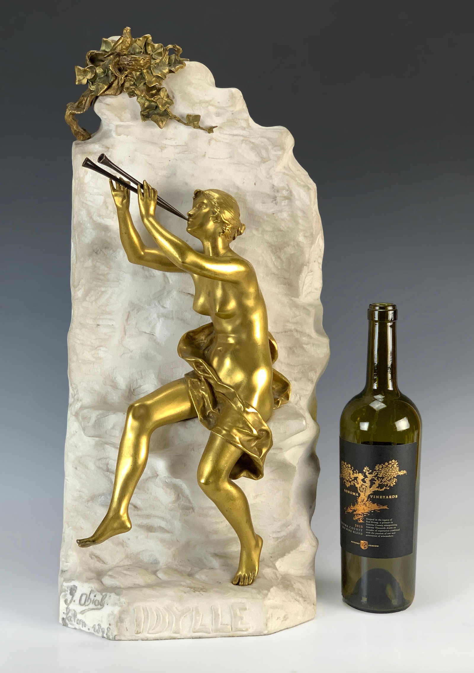 Gustavo Delgado Idylle Marble & Bronze Sculpture: Gustavo Obiols Delgado (1858-1910). Titled "Idylle", Dated Salon 1892, Beautiful gilt bronze nude figure with two flutes, mounted upon a white marble wall, topped with gilt bronze bird and nest, signe
