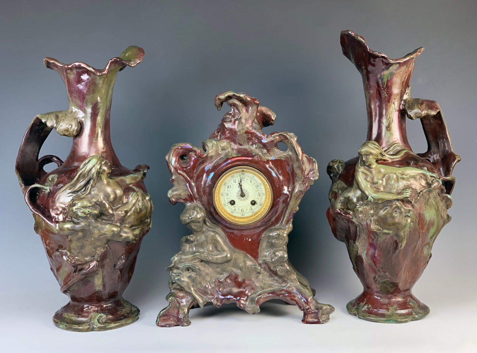 Alfred Renoleau Art Nouveau Garniture Clockset: Alfred Renoleau (France 1854-1930) Art Nouveau 3 piece ceramic clock garniture set, earthy shades of red, brown and green with iridescent reflections. Clock decorated with a Naiad on a chimerical anim