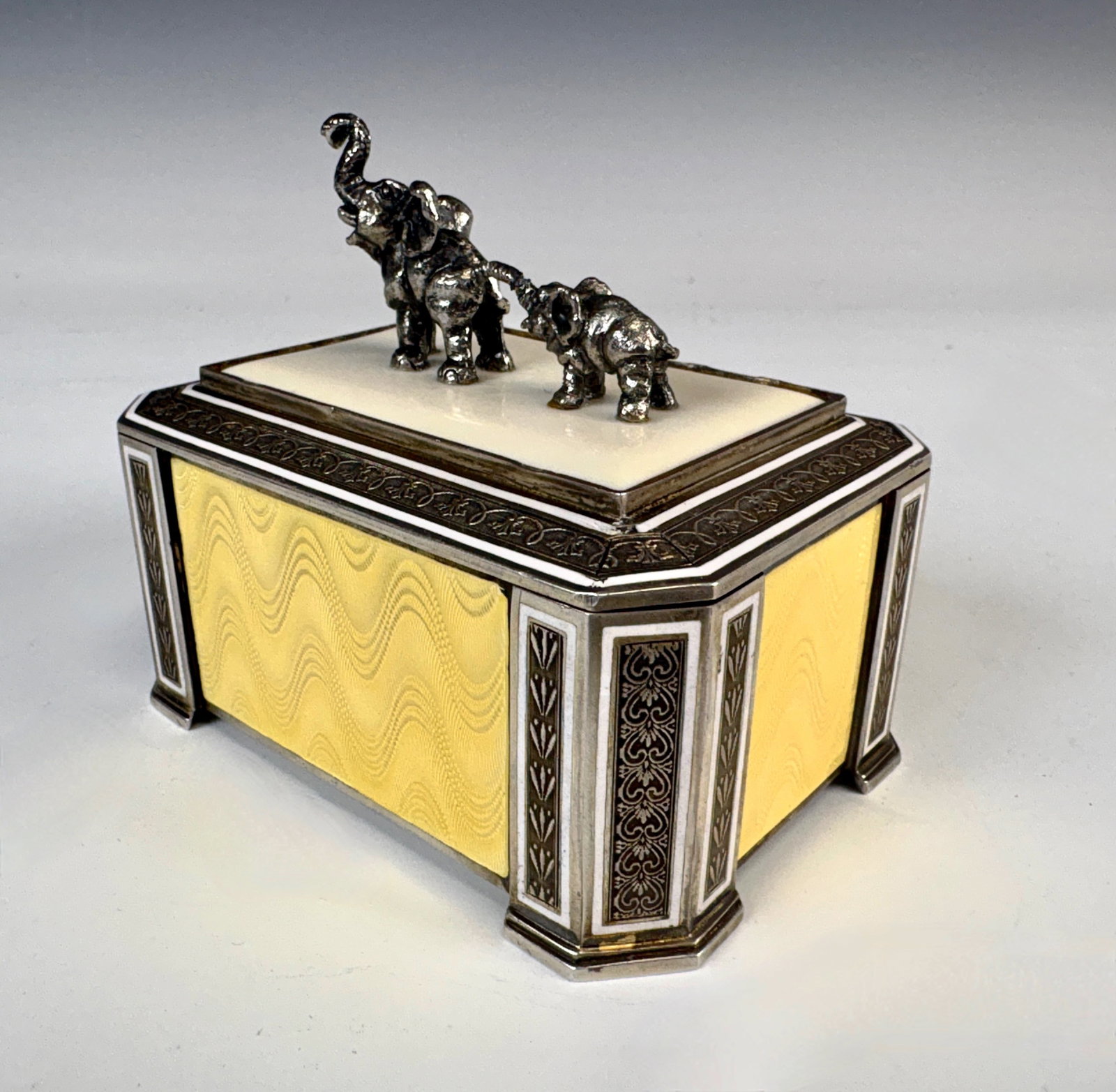 Swedish Sterling & Guilloche Enamel Box w Elephant: A fine Swedish sterling silver and soft yellow guilloche enamel lidded box topped with two silver elephant figures and black enamel embellishment on the corners, interior with gold wash, hallmarks wit