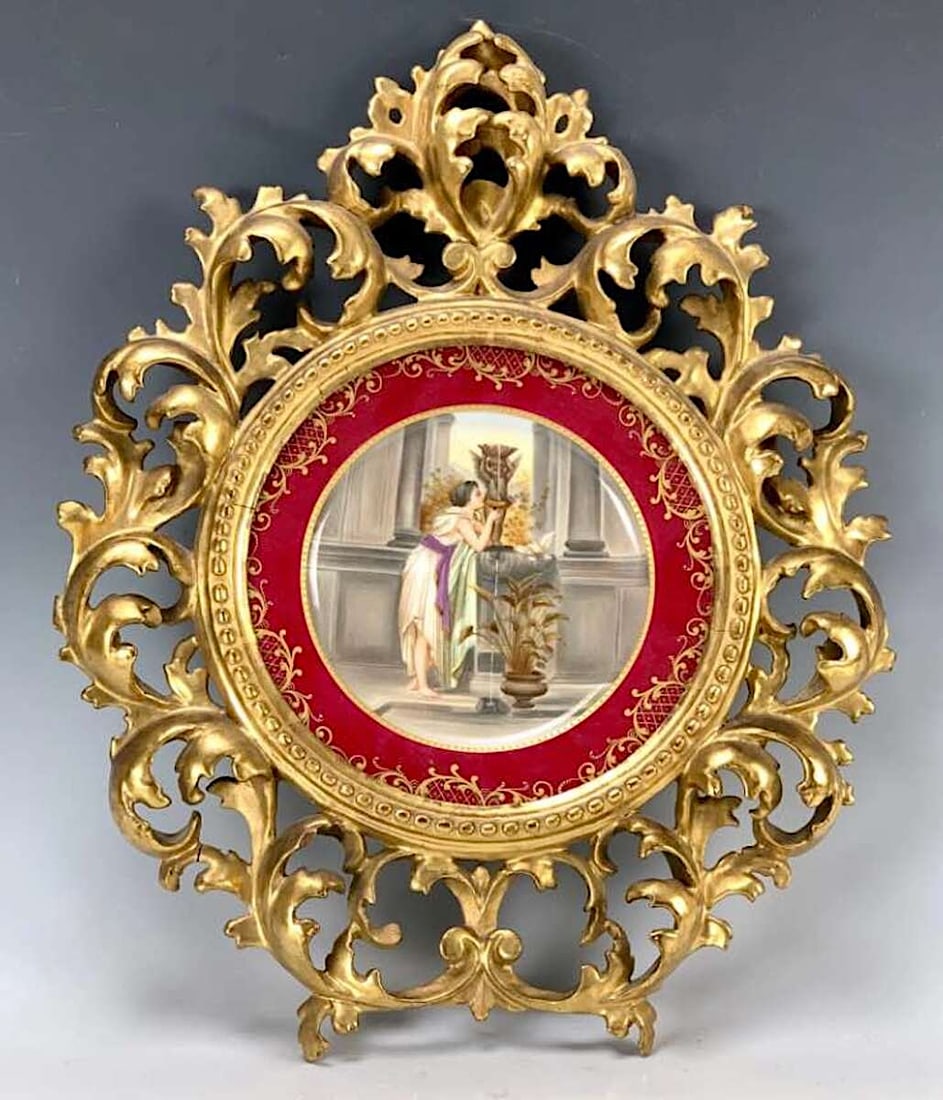 Royal Vienna Hand Painted Plate w/ Ornate Frame: Fine hand painted porcelain plate depicting a young lady getting a drink at a fountain, red border with gold gilt design, mounted in a beautiful Florentine round frame, marked with Beehive and Austria