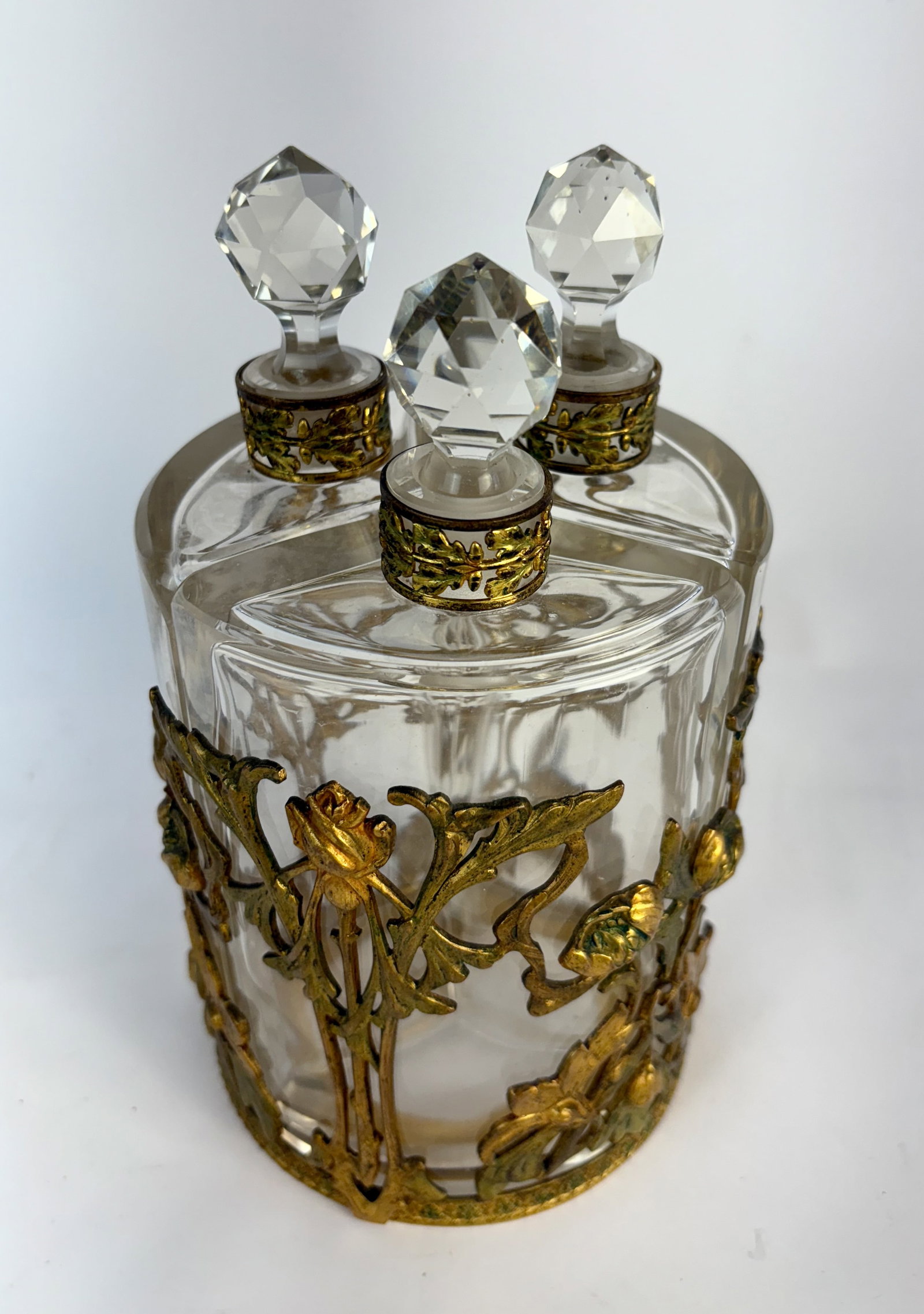 Large Nouveau Gilt Bronze & 3 Glass Perfume Bottle: Circa 1900, a large art nouveau vanity set of gilt bronze and 3 glass perfume or cologne bottles, each clear glass bottle with matching faceted stoppers, bottles fitted into art nouveau floral decorat