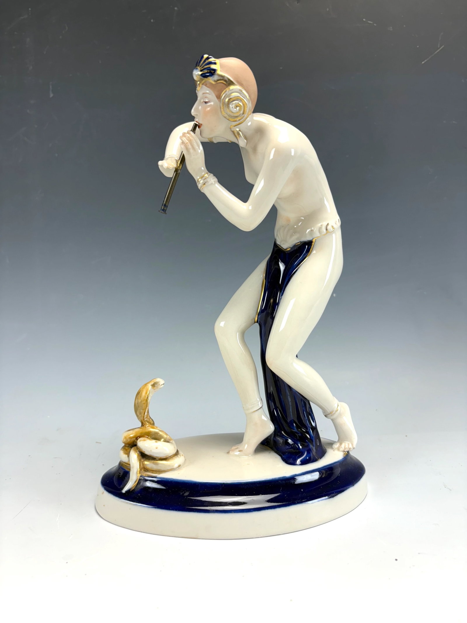 Royal Dux Nude Snake Charmer Porcelain Figurine: A handpainted glazed porcelain figure of a partially clad female snake charmer with a horn and a cobra, signed with applied pink triangle, very good condition, 10.24" tall