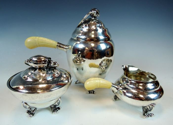 Georg Jensen (1925-1930) "Blossom" Silver Tea Set: Designed 1919, with bone handles marked sterling and makers mark model 2A. Teapot measures 6 1/4" x 6 1/4", creamer 2 1/4" x 5 1/4", and covered sugar 3 3/4" x 3 3/4", total weight 24.444 ounces. Esti