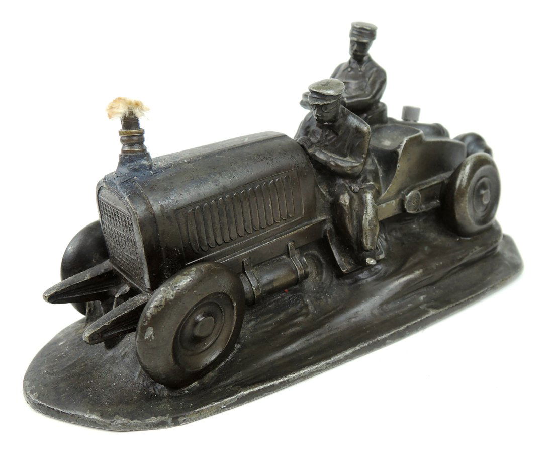 Rare Automobile Cigar Lighter: Circa 1910, an unusual cigar lighter modeled as an antique car with a driver and his assistand, having a wick which protrudes from the top of the radiator and a wand placed on rear trunk, of a white m