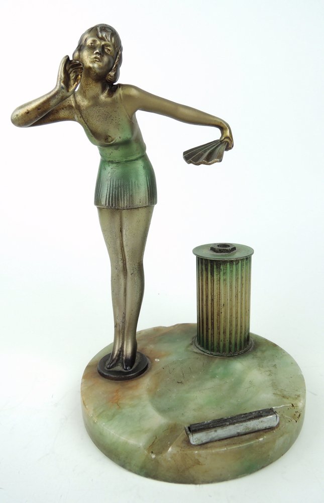 Art Deco Figure of Young Woman Cigar Lighter: Circa 1920, posed as if smoking, a polychromed metal figurine of a scantily clad young woman in holding a fan alongside a column which would have originally held a wand (missing), mounted on circular 