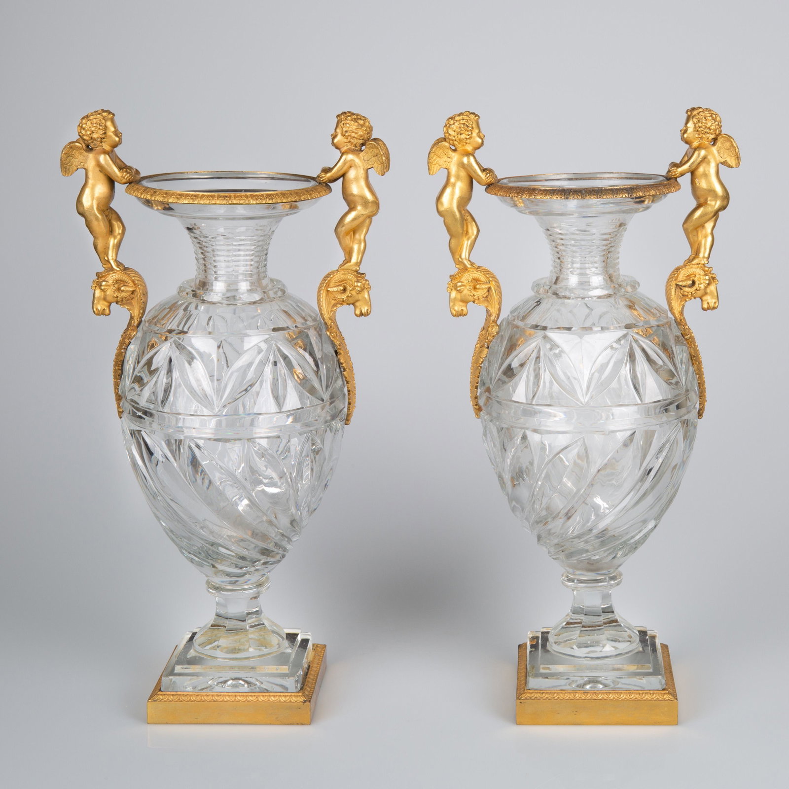 A PAIR OF FRENCH OR RUSSIAN ORMOLU-MOUNTED TWO-HANDLED: A PAIR OF FRENCH OR RUSSIAN ORMOLU-MOUNTED TWO-HANDLED CRYSTAL VASES, 19TH CENTURY each of baluster form, the body partly gadrooned, surmounted with handled formed as putti leaning, with arms crossed,