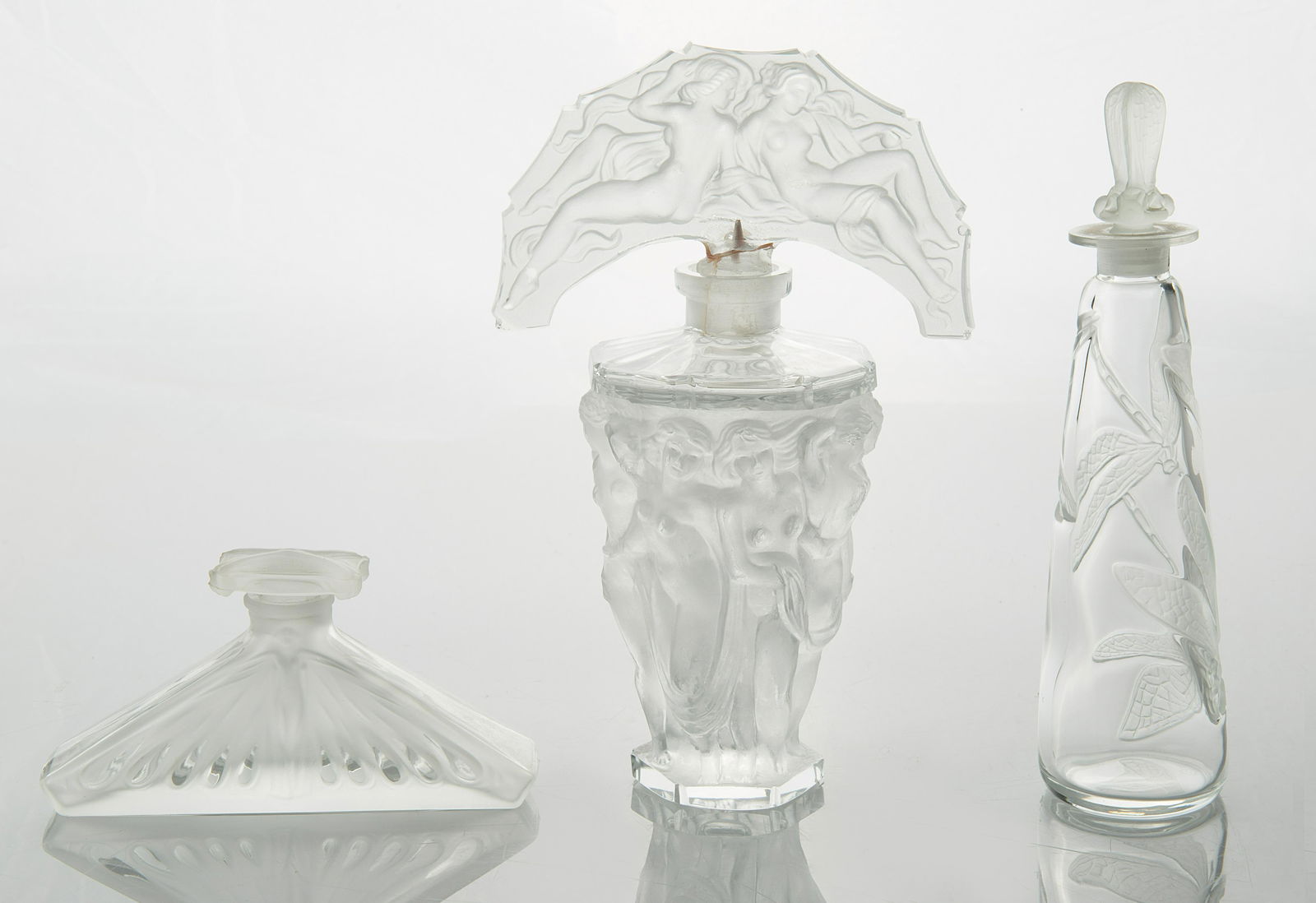 GROUP OF THREE GLASS PERFUME BOTTLES: GROUP OF THREE GLASS PERFUME BOTTLES comprising: a) BROSSE "FEMMES AILEES" PERFUME BOTTLE AFTER LUCIEN GAILLARD, REPRODUCED FOR THE METROPOLITAN MUSEUM OF ART, 1986, after 1913 design the body of tr