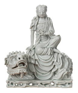 A DEHUA FIGURE OF GUANYIN SEATED ON A LION: A DEHUA FIGURE OF GUANYIN SEATED ON A LION seated on a recumbent lion with one leg raised, the goddess dressed in long flowing robes opening at the chest to reveal a beaded necklace, her plump face wi