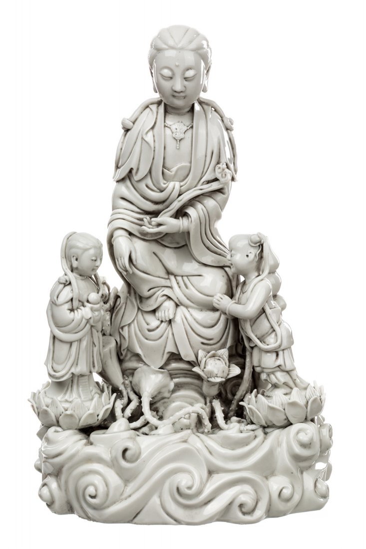A BLANC-DE-CHINE FIGURE OF GUANYIN ON A ROCK WITH TWO: A BLANC-DE-CHINE FIGURE OF GUANYIN ON A ROCK WITH TWO ATTENDANTS , the deity is depicted seated on the rock above waves, with her robe falling gracefully, in her left hand she holds a ruyi scepter, su