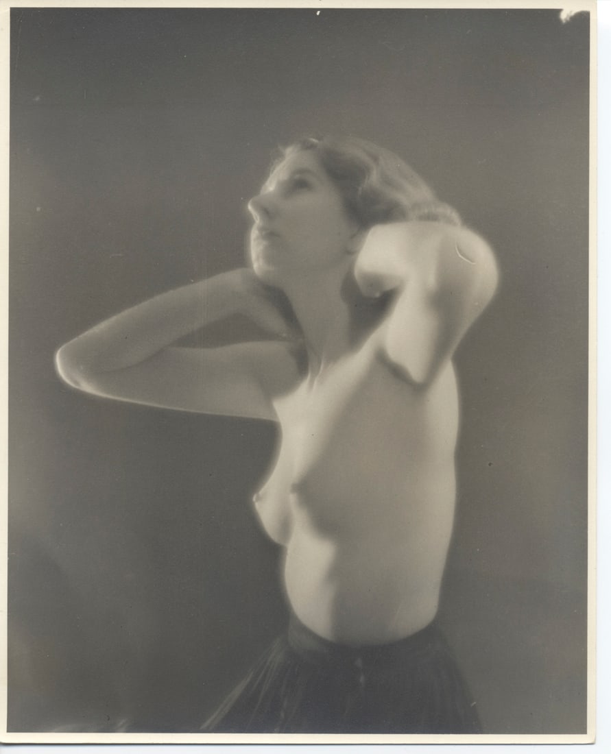 Vintage Artistic Nude Photography: Photograph measures 8x10 inches and features a vintage style black and white photograph of a woman posing nude, with her left arm raised to her head, creating an elegant silhouette against a soft-focu