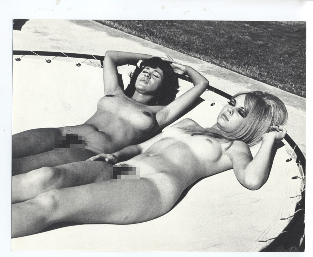 Vintage Artistic Nude Photography: This is an 7 x 9.5 inch black and white photograph featuring a woman posing on a lounge chair in a nudist camp setting. She is lying back with her arms raised behind her head, showcasing a relaxed pos