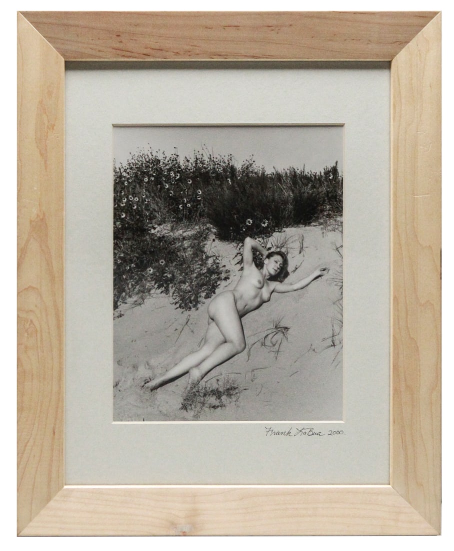 Nature's Embrace: Titled "Nature's Embrace," this framed black and white photograph, measuring 17 x 14 inches, captures a woman's harmonious connection with the natural world. She reclines gracefully in a sandy clearin