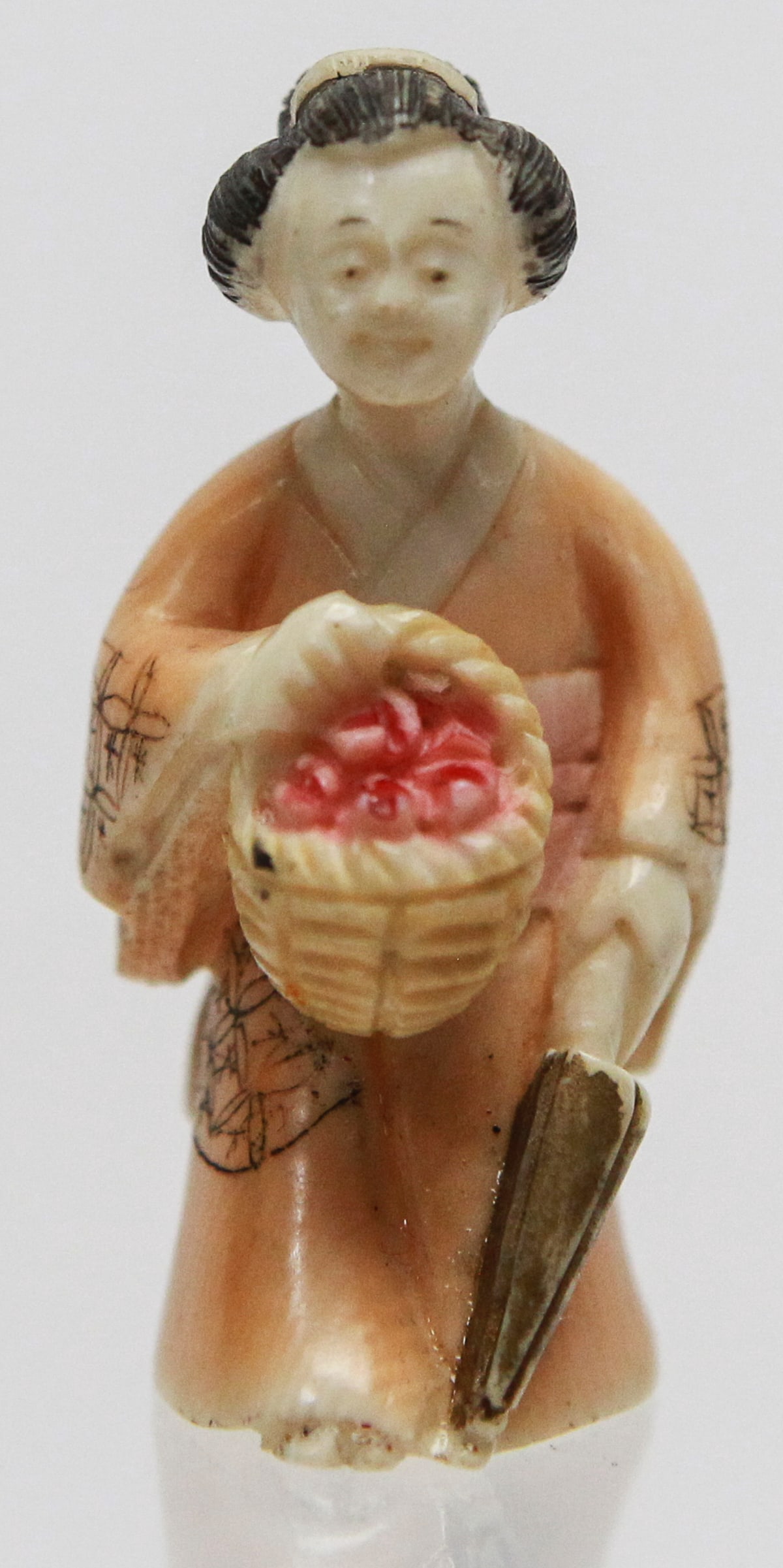 Vintage Japanese Carved Polychrome Netsuke of Woman with Basket of Peaches: Vintage Japanese carved polychrome netsuke depicting a young woman in a finely detailed kimono carrying a woven basket filled with red peaches in one hand and a folded umbrella in the other. The figur