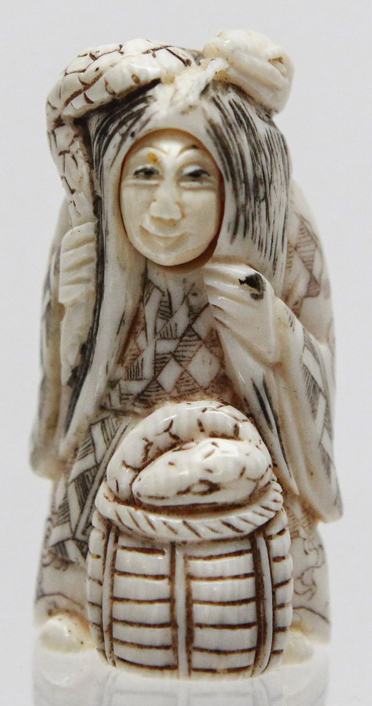 Vintage Japanese Carved Netsuke of Otafuku (Okame) with Transforming Hannya Mask: Vintage Japanese carved netsuke depicting Otafuku (Okame) carrying a basket with a hidden transforming Hannya mask face. The finely carved figure features a movable facial insert that changes expressi