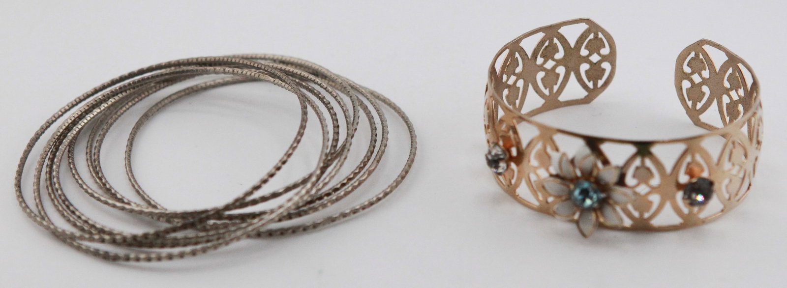 Lot of 2 Vintage Bracelets: Collection of two vintage fashion bracelets. Includes a set of slender silver-tone textured bangle bracelets and an openwork gold-tone cuff bracelet featuring a pierced heart motif accented with white