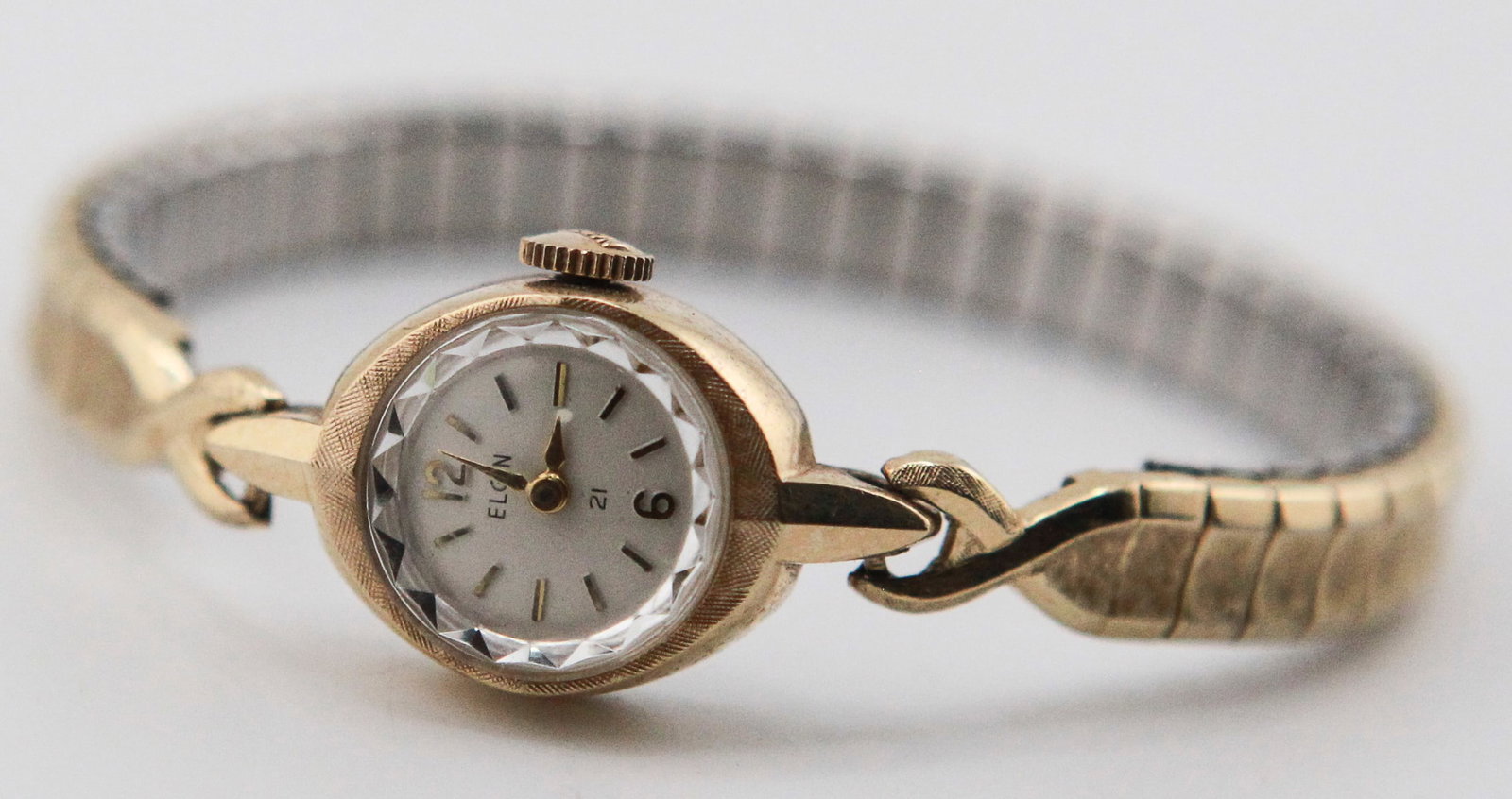 Elgin Ladies Gold-Tone Wristwatch: Vintage Elgin ladies wristwatch with gold-tone case, silver-tone dial, Arabic numerals at 12 and 6, baton hour markers, and faceted crystal. Fitted with a gold-tone expansion bracelet. Stainless