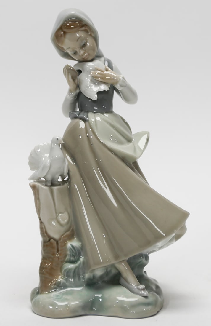 Lladró Girl with Doves Porcelain Figurine: Lladró glazed porcelain figurine depicting a young woman in a headscarf and flowing dress gently holding a dove, with another bird perched beside her on a rustic tree stump. Rendered in the