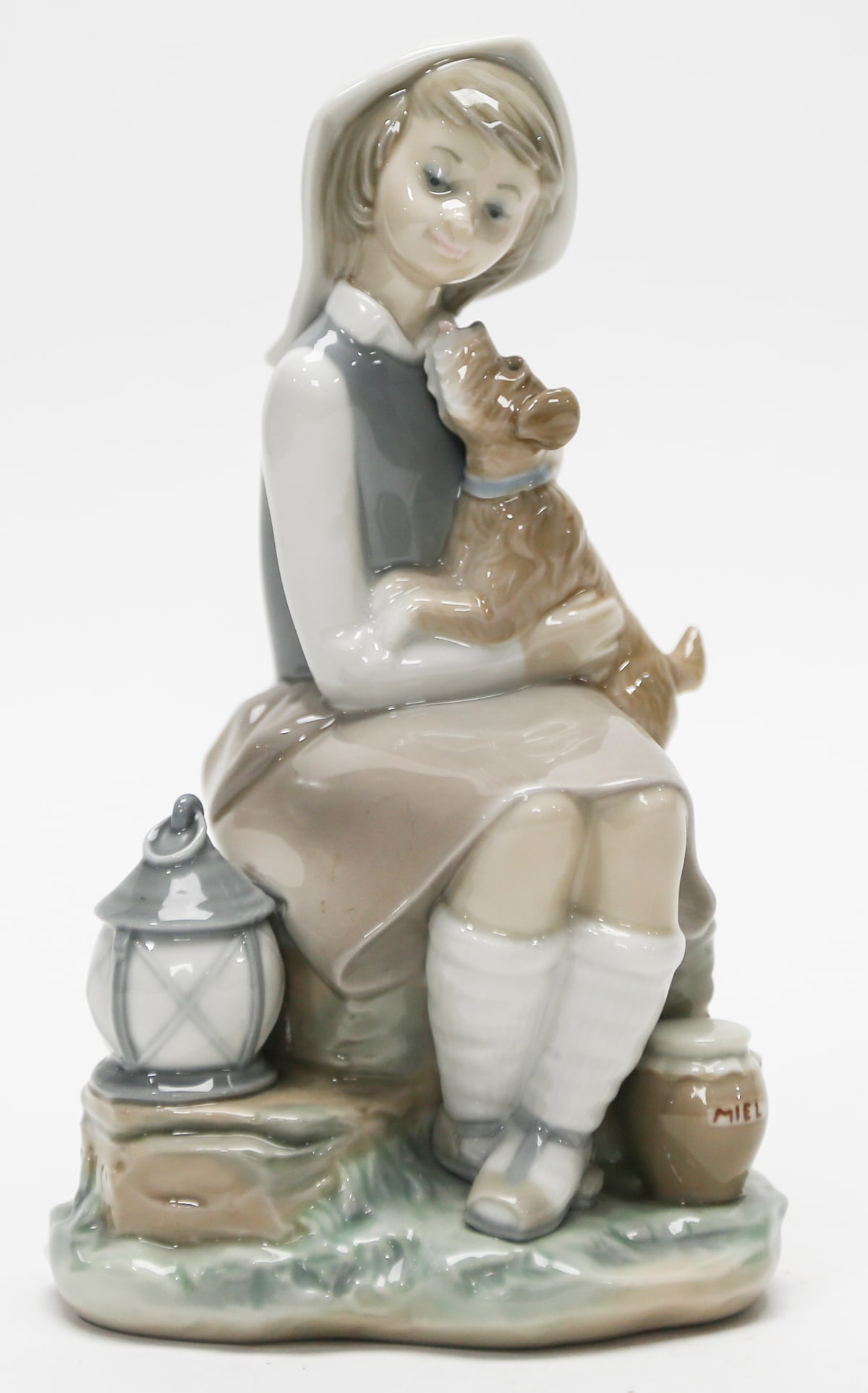 Lladró Girl with Dog Figurine: Lladró glazed porcelain figurine depicting a seated young girl affectionately holding a small brown dog. The charming scene includes a lantern and honey jar beside the figure, with softly modeled