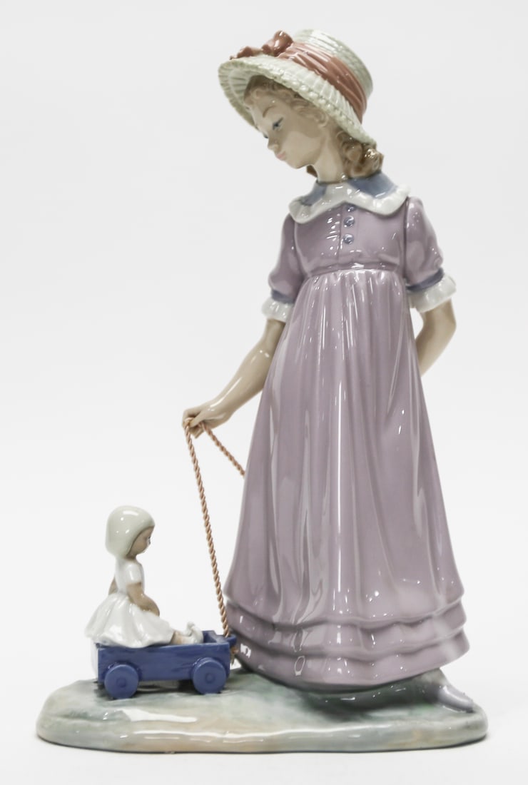 Lladró Mother Pulling Child in Wagon Figurine: Charming Lladró porcelain figurine depicting a mother in a lavender dress and ribbon-trimmed bonnet pulling a small child seated in a blue wagon. The softly glazed pastel palette, sculpted clothing