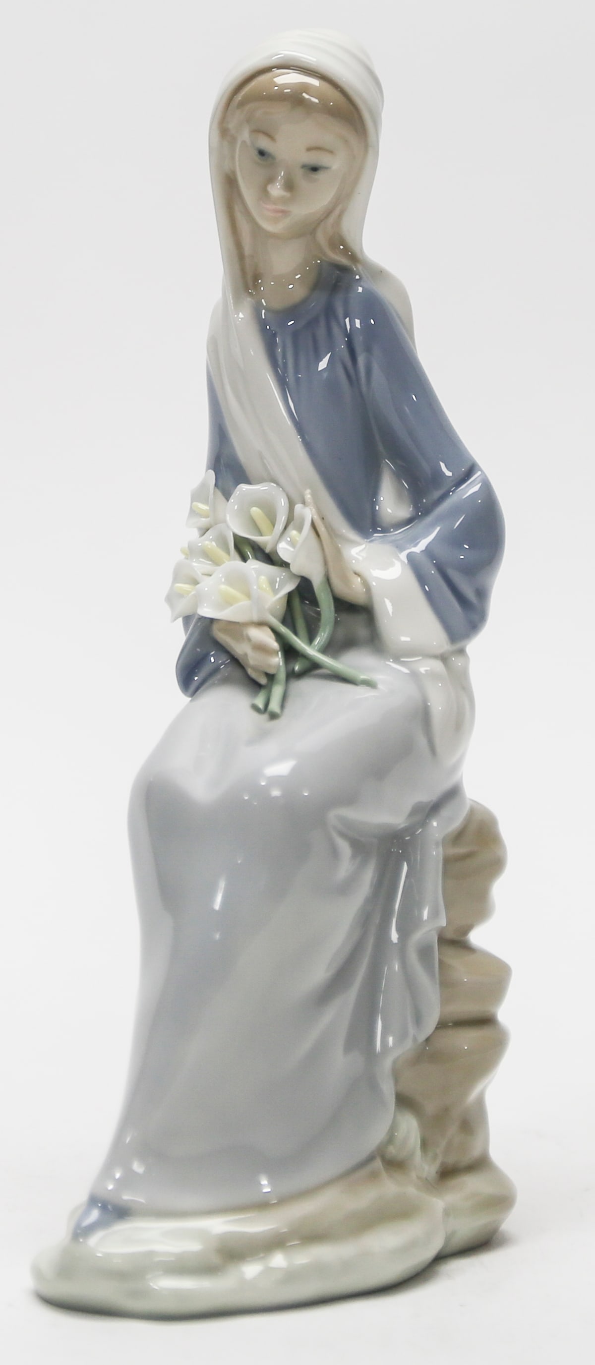 Lladró Madonna with Lilies Porcelain Figurine: Graceful Lladró porcelain figurine depicting the seated Madonna holding a bouquet of white calla lilies. Finished in soft blue, gray, cream, green, and earth tones with the characteristic glossy